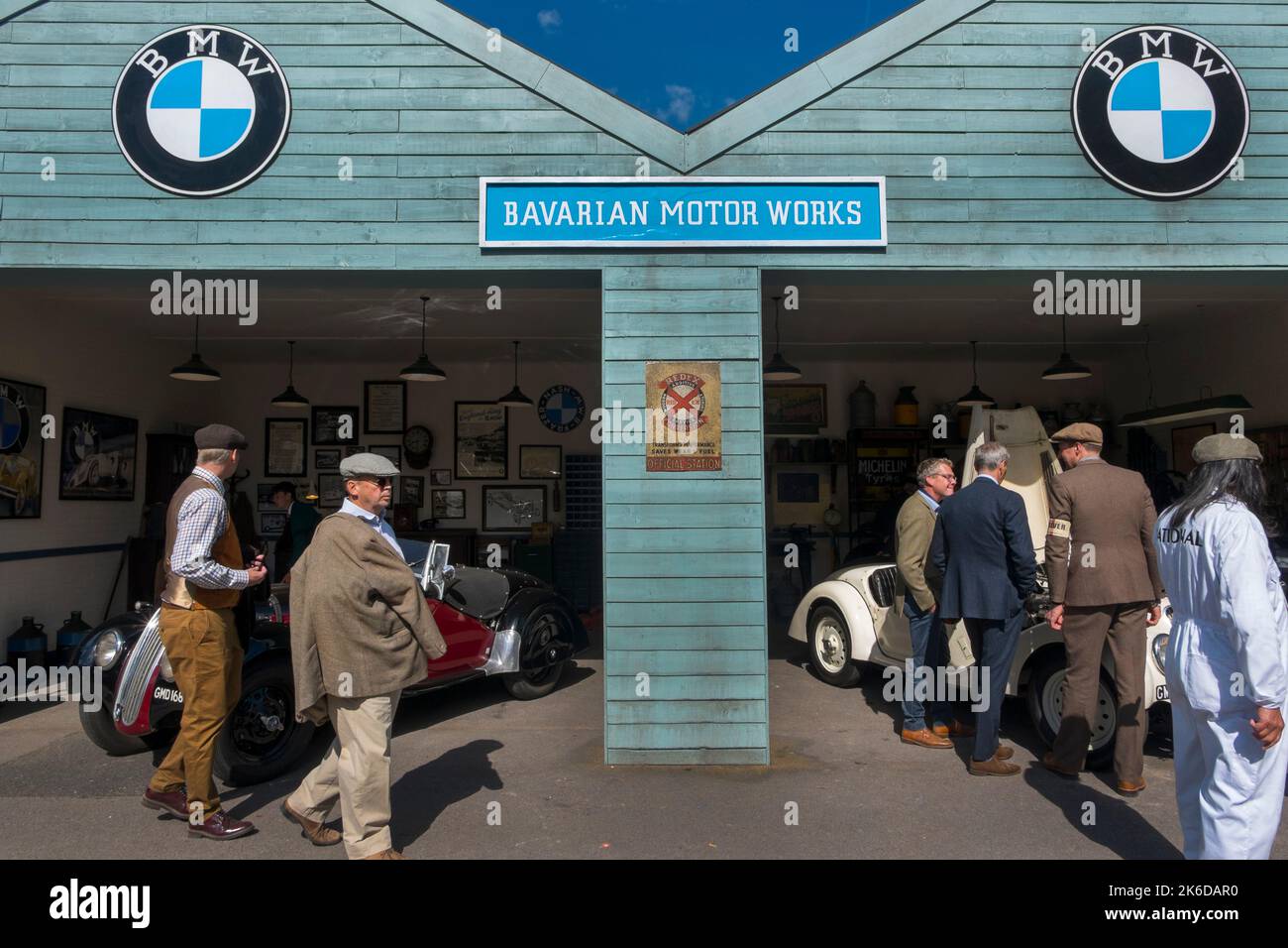 Menschen, die in Vintage-Kleidung gekleidet waren, schauten sich die Frazer Nash BMW-Autos in der Garage des Bayerischen Motorwerks, BARC Revival Meeting, Goodwood, Großbritannien, an Stockfoto