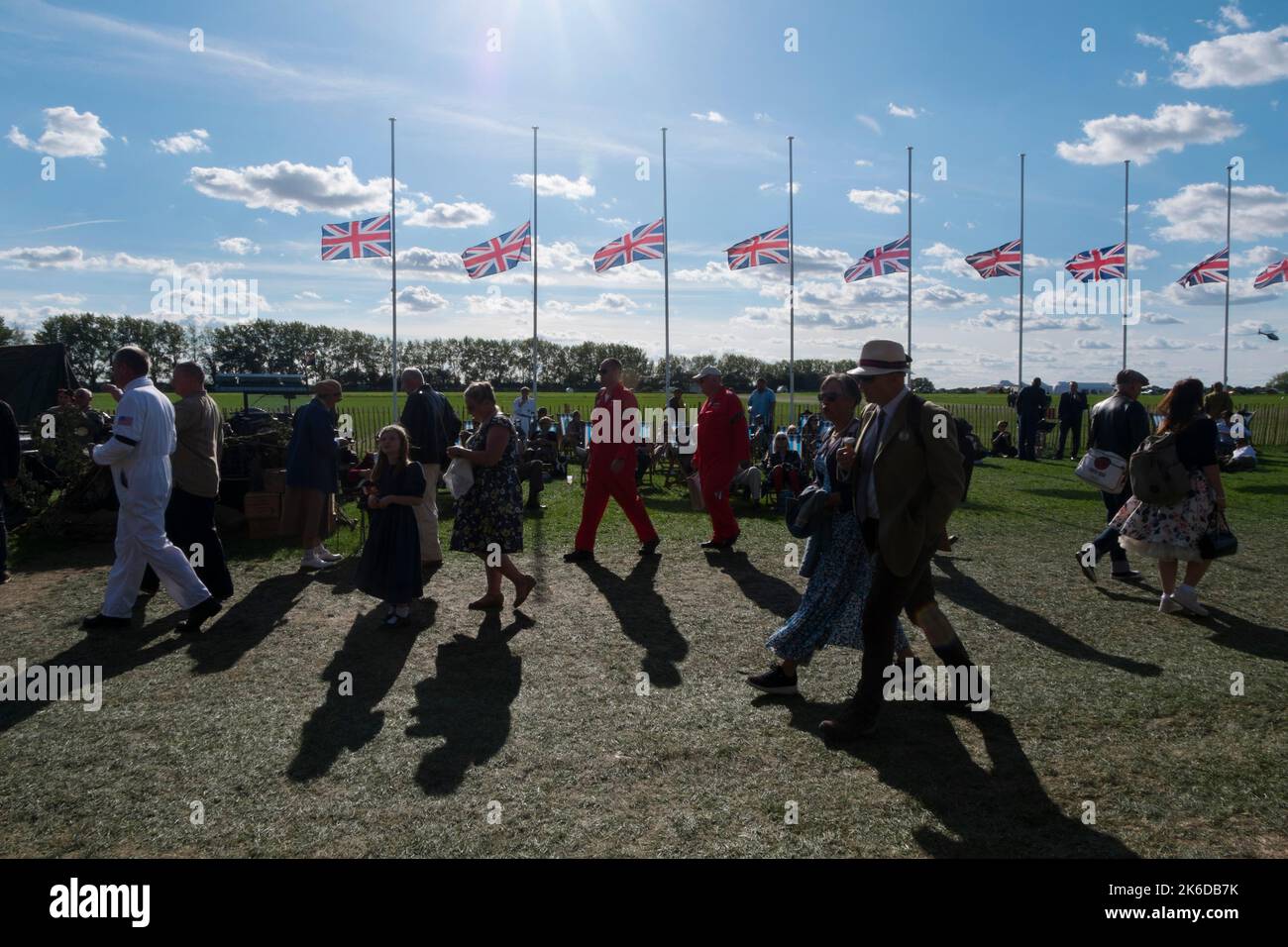 Menschen aus der Zeit kleiden sich auf dem Spielfeld mit Union Jack-Flaggen hinter dem Halbmast in Bezug auf den Tod der Königin, BARC Revival Meeting, Goodwood Stockfoto