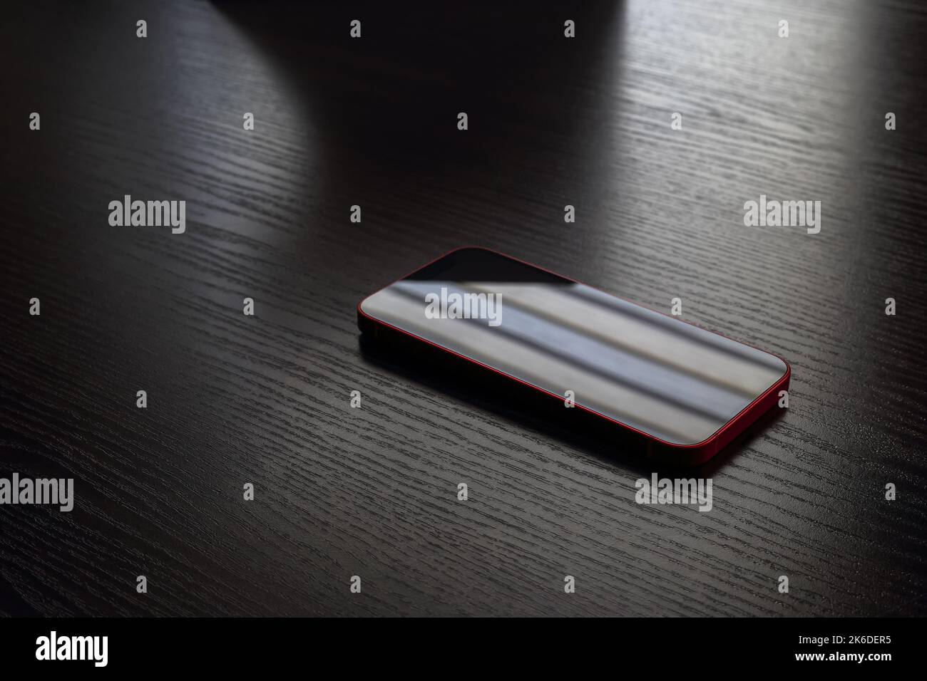 Rotes kleines Mobiltelefon, das in einem dunklen Raum auf einem Tisch liegt Stockfoto