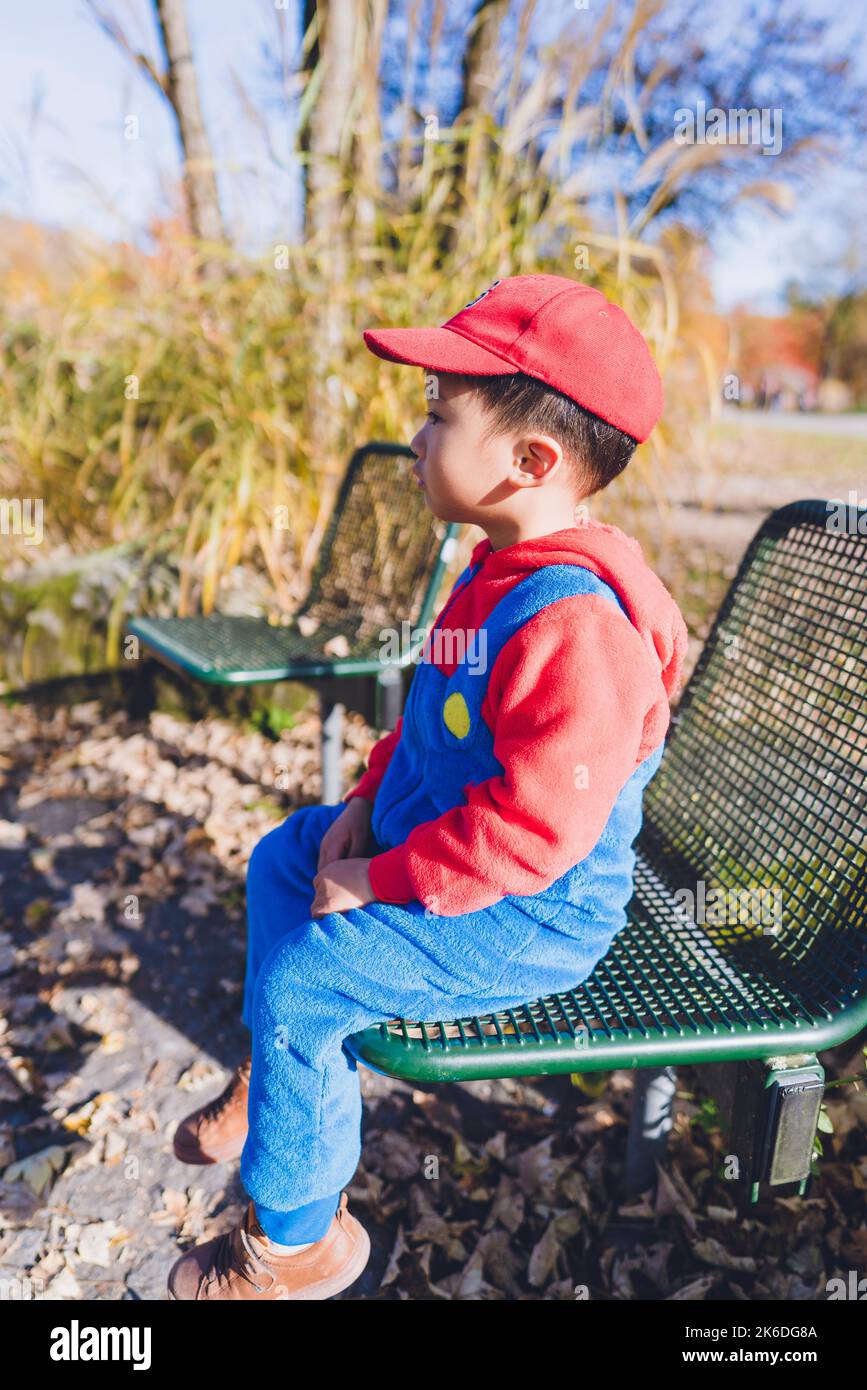 Ein in Kostüm gekleideter Junge sitzt auf einer Bank in einem öffentlichen Park. Stockfoto