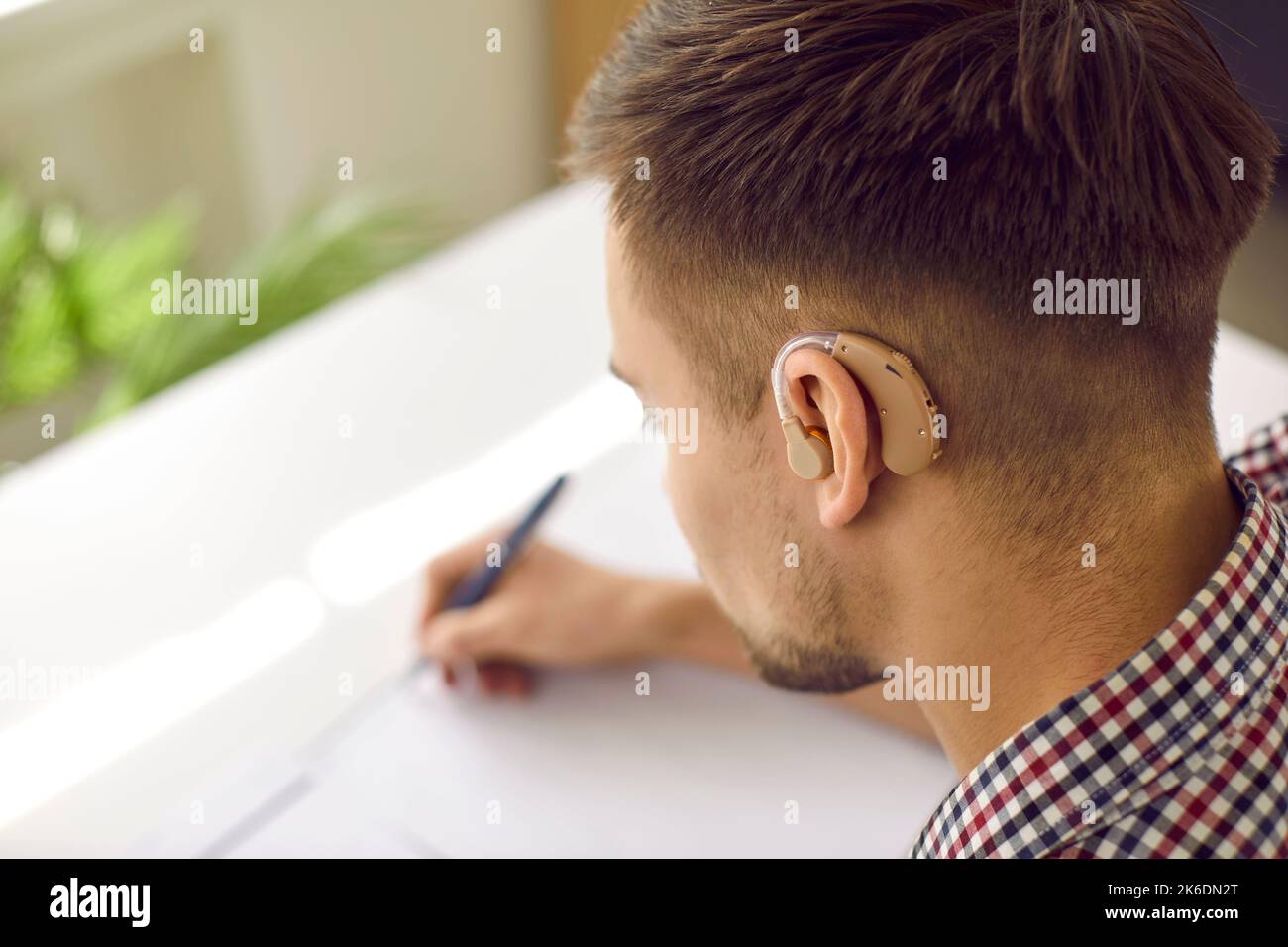 Hörgeschädigte Studenten, die ein modernes Hörgerät tragen, sitzen am Schreibtisch und schreiben Stockfoto