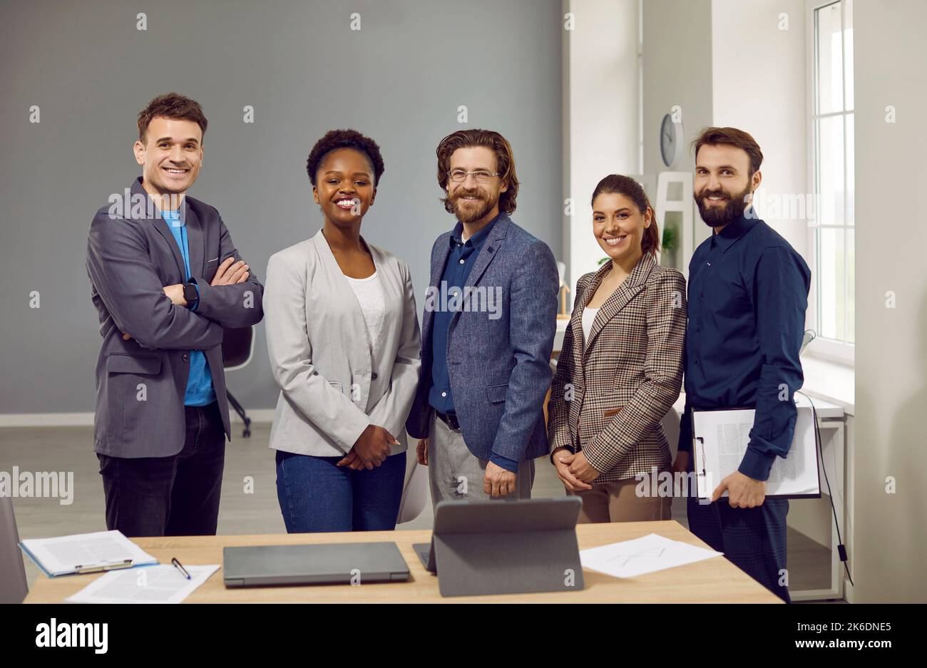 Multiethnische Personen im Vorstand von Unternehmen oder Unternehmen stehen mit einem Lächeln neben dem Tisch Stockfoto