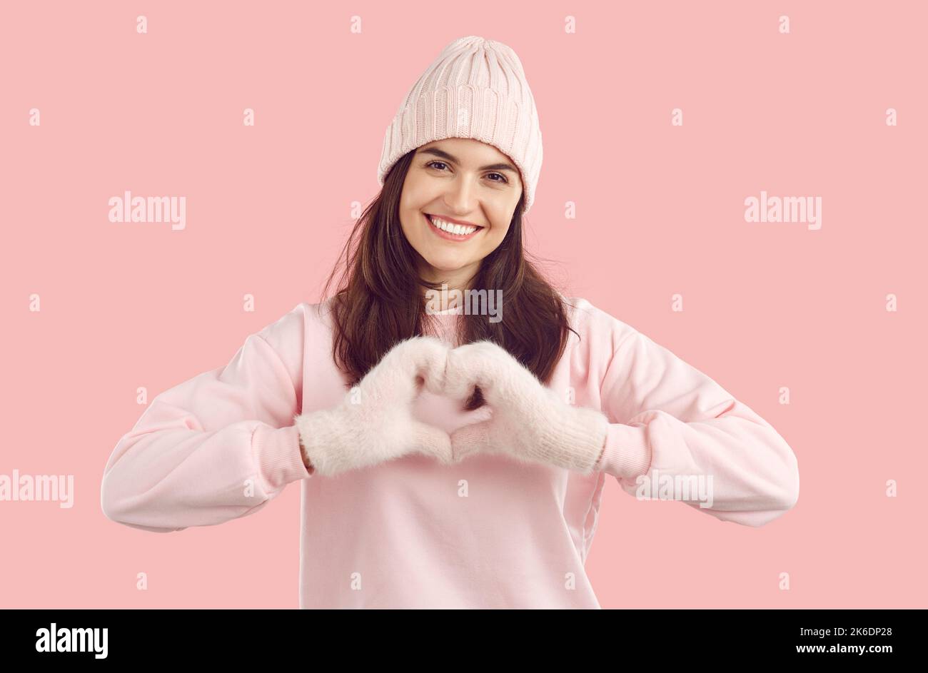 Glückliche Frau in rosa warmen Winterhut und Fäustlingen bildet Herz mit Händen als Liebessymbol Stockfoto