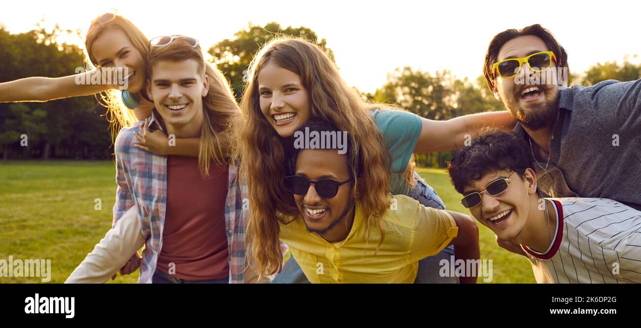 Gruppe von fröhlichen jungen Freunden, die Spaß mit Huckepack im Freien im Park am Sommertag. Stockfoto