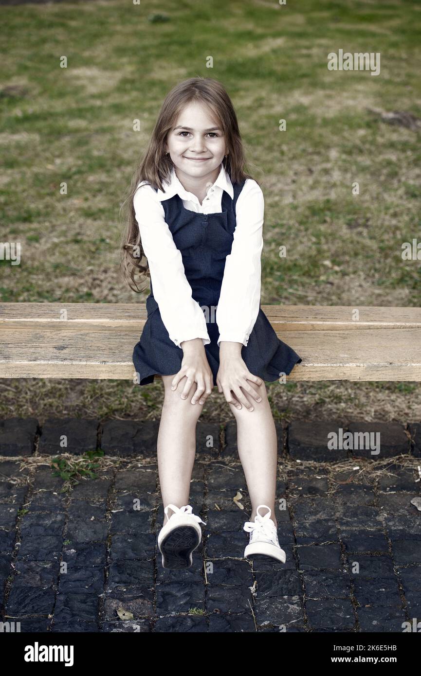 Denn dein kleines Kind hat es verdient. Glückliches Kind sitzen auf der Bank im Freien. Schule aussehen des Kindes Mädchen. Formelle Mode. Uniformkleid. Grundschulbildung. Chi Stockfoto