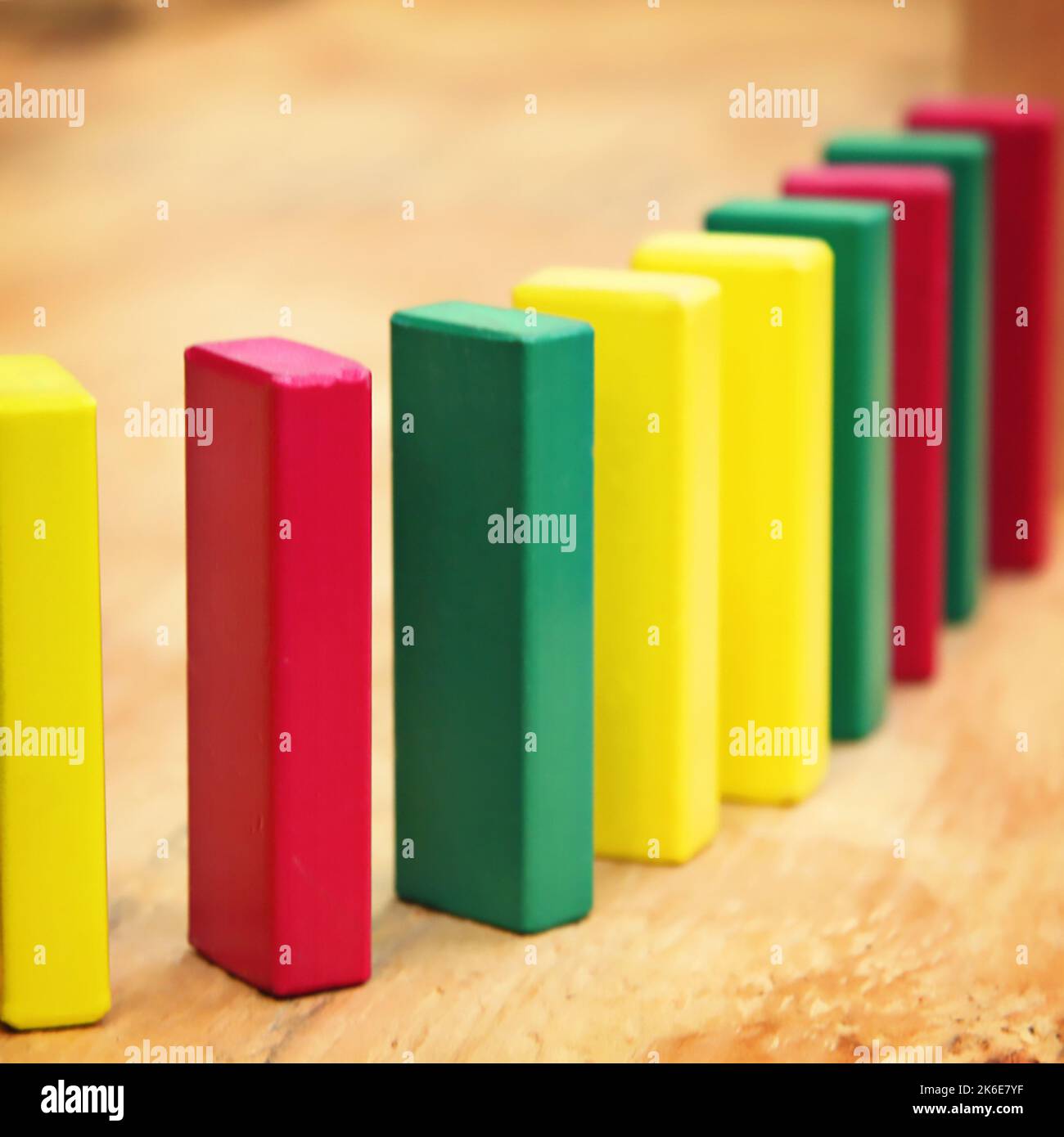 Holzbausteine für einen Vorschulunterricht oder ein Kind stehen in Rot, Gelb und Grün auf, um eine Reihe zu bilden und fallen wie Dominosteine nach unten Stockfoto