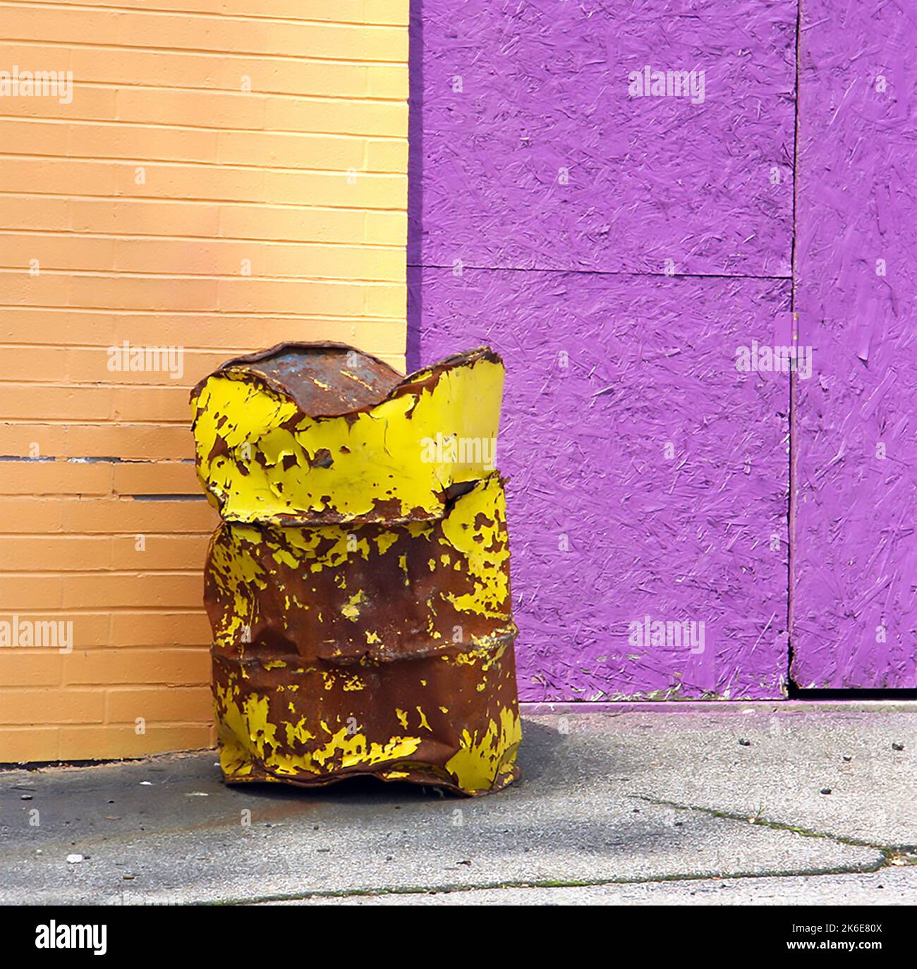 Ein großer, gelber, mit Rost übersäter Metallmüll sitzt an einer purpurnen Pfirsichwand und erzeugt auf einer verlassenen Mitte einen Farbblock Stockfoto