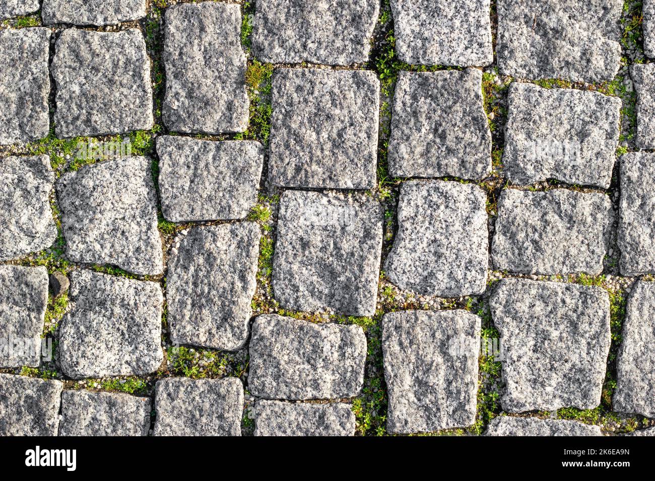Steinstraße gepflastert mit asymmetrischen Steinen mit gesproßenem Gras an den Nähten. Texturierter Hintergrund, Draufsicht Stockfoto