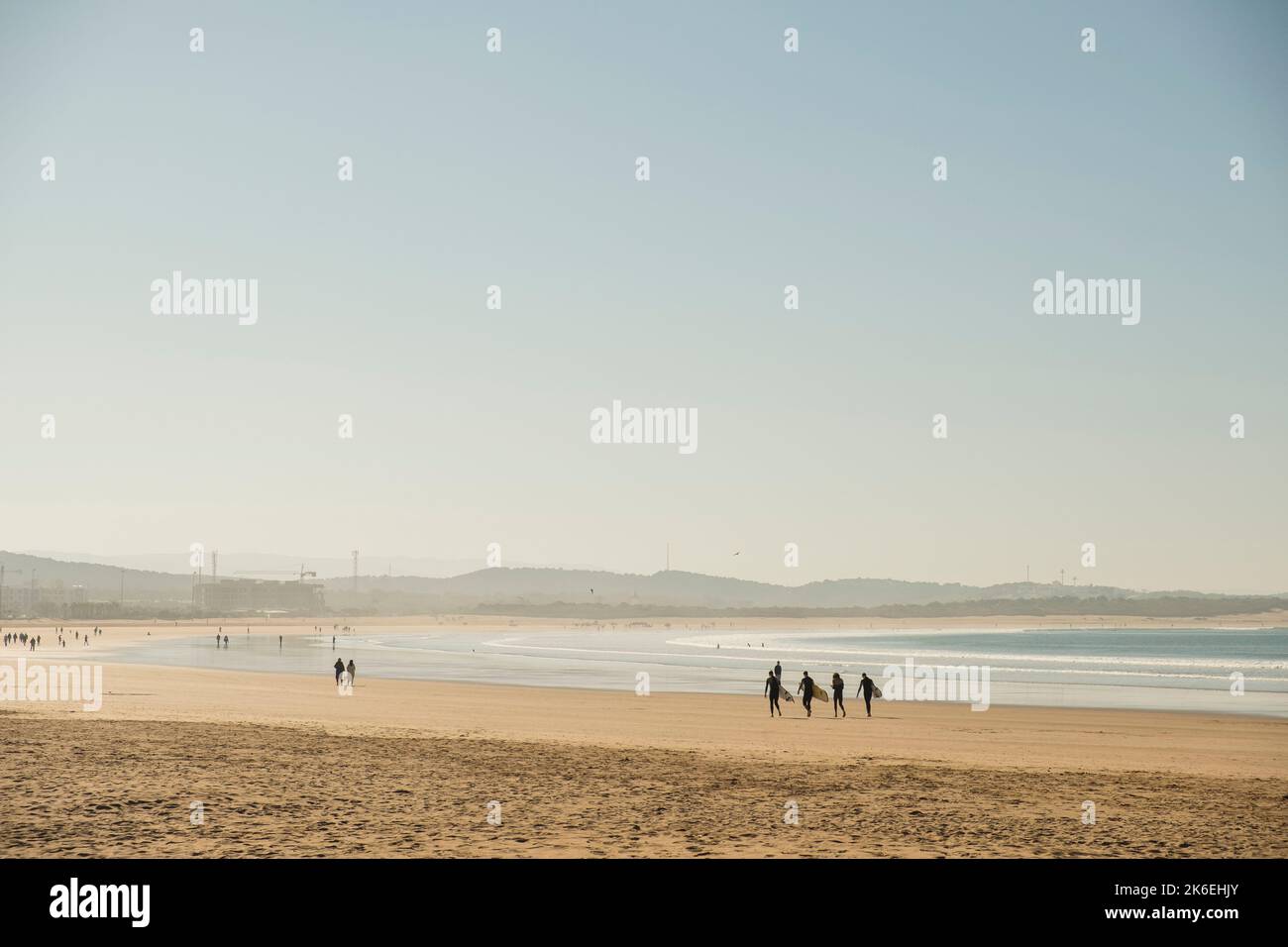 Vier Surfer tragen Surfbretter am goldenen Sandstrand von Essaouira in Mogador Bay, Marokko, Nordafrika Stockfoto