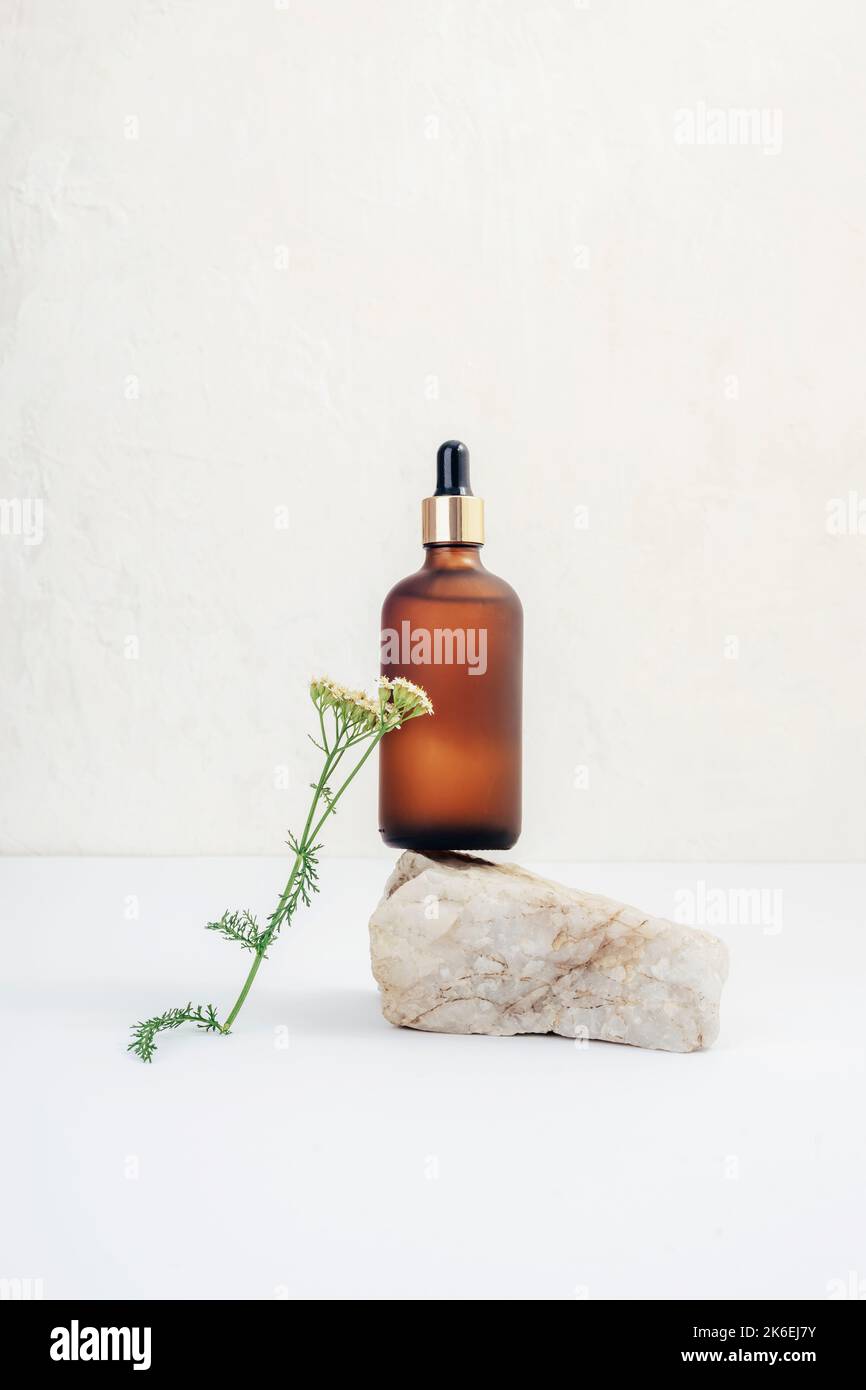Braune Kosmetiköl- oder Serumflasche, Naturstein und Schafgarbe-Blume auf weißem Hintergrund. Naturkosmetik, Spa- und Wellnesskonzept. Stockfoto