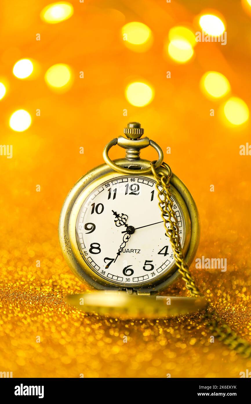 Weihnachtstapete. Goldene Uhr in Gold Glitter auf einem gelben Hintergrund mit leuchtenden Bokeh.Urlaubszeit.Feiertagslichter.schöne Weihnachtshintergrund Stockfoto
