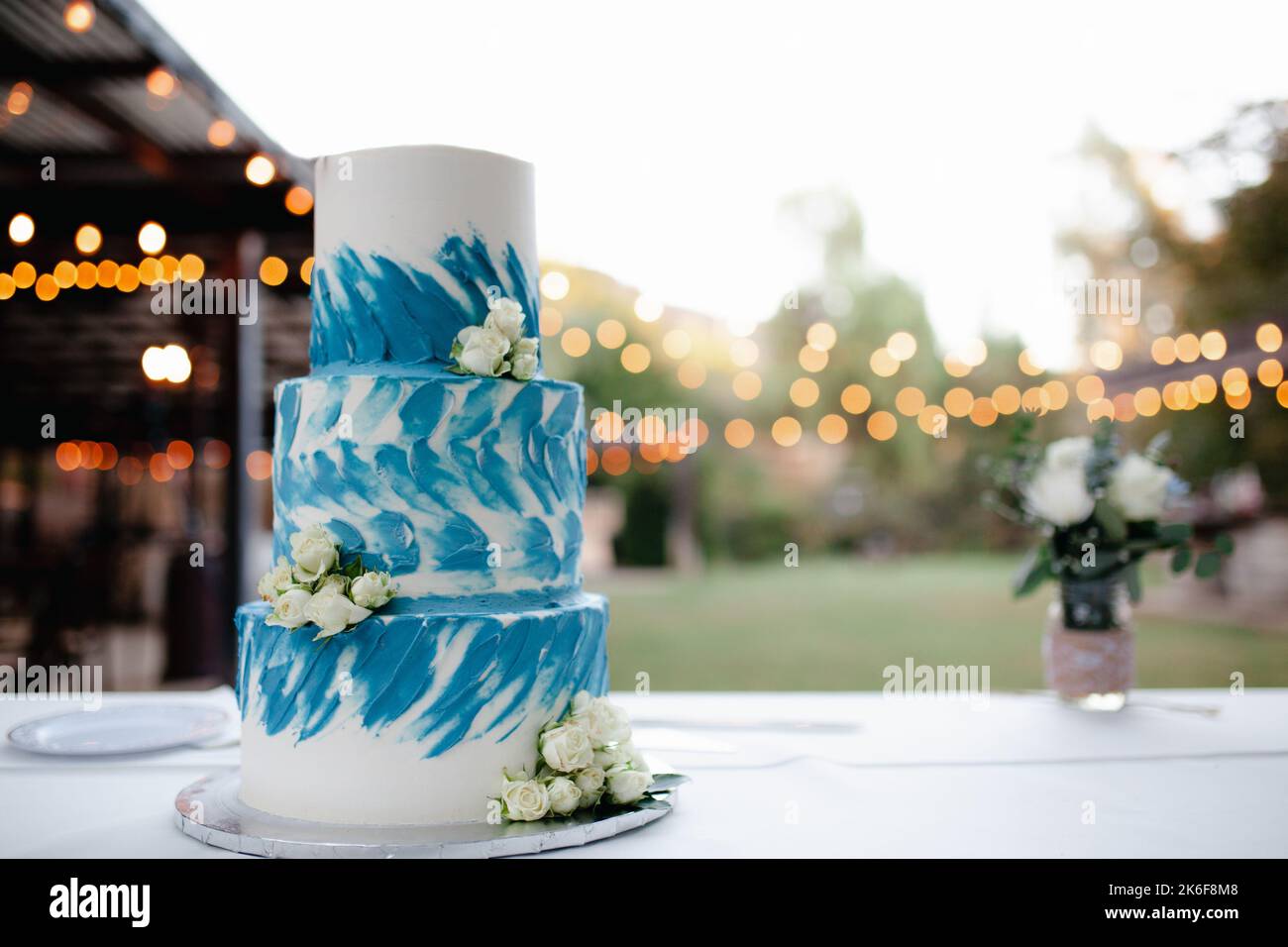 Dreistufige weiße und blaue Hochzeitstorte mit weißen Rosen und Herztopper. Stockfoto