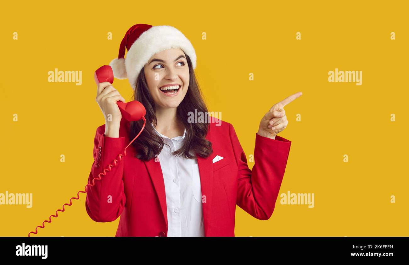 Lächelnde junge Weihnachtsfrau mit dem Hörer, der den Zeigefinger zur Seite auf den leeren Werbeplatz zeigt. Stockfoto