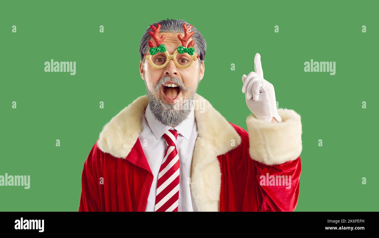 Glücklicher bärtiger Mann in lustigen Weihnachtsgläsern und Weihnachtsmantel hat eine gute Idee und zeigt den Finger nach oben Stockfoto