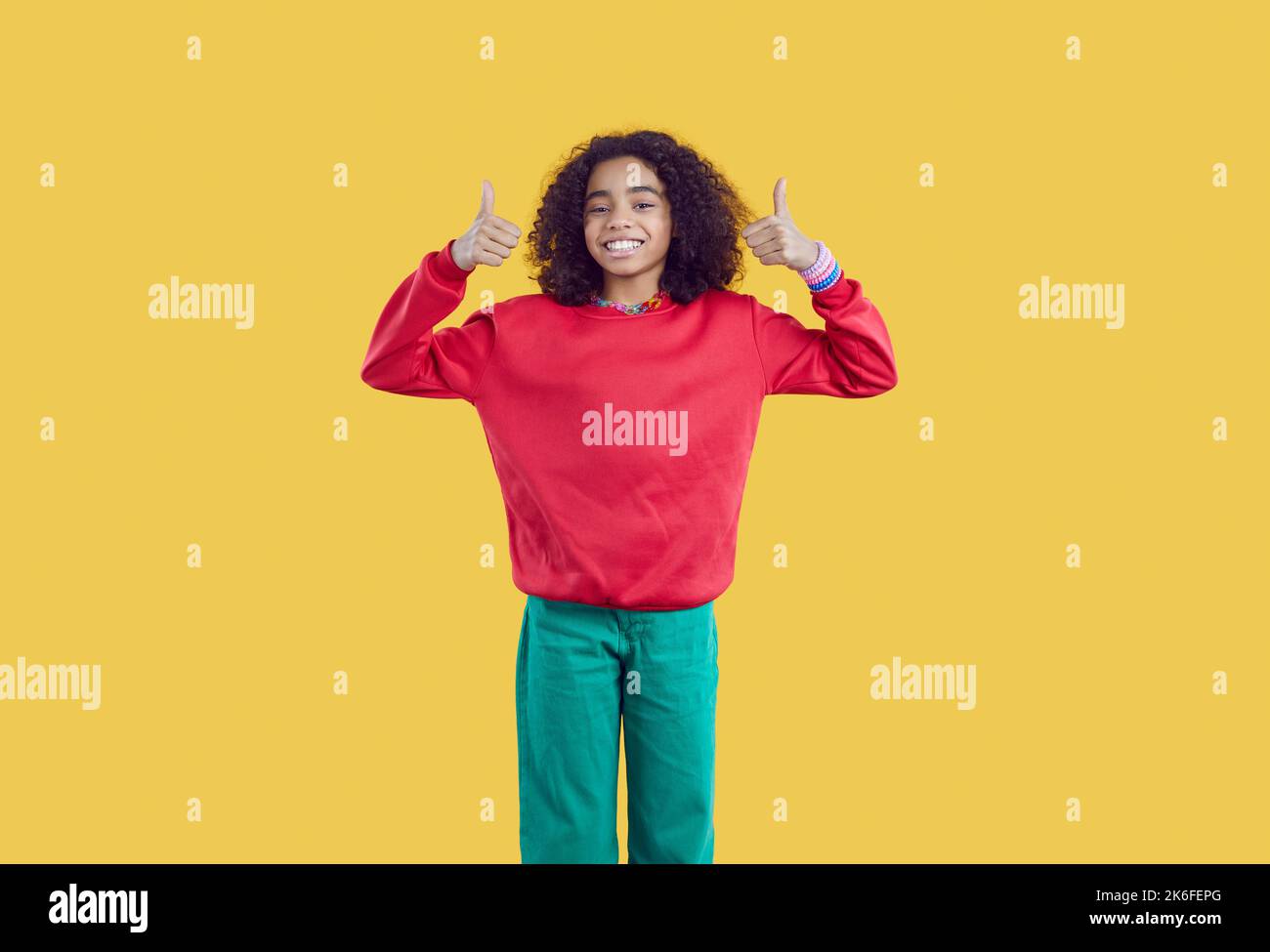 Happy african american preten Mädchen auf gelbem Hintergrund zeigt Daumen nach oben empfehlen beste Wahl. Stockfoto