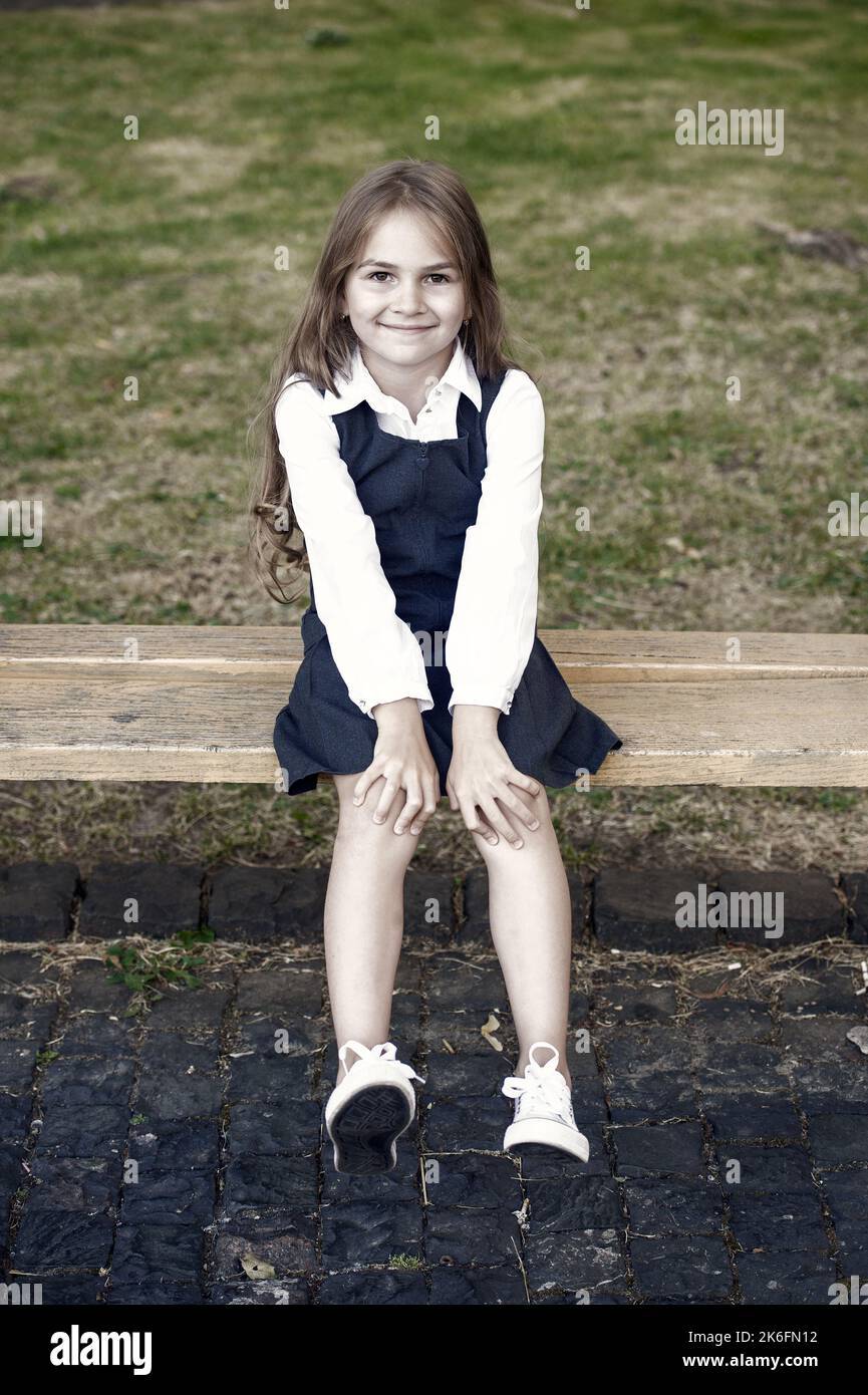 Denn dein kleines Kind hat es verdient. Glückliches Kind sitzt auf der Bank im Freien. Schule aussehen des Kindes Mädchen. Formelle Mode. Uniformkleid. Grundschulbildung Stockfoto