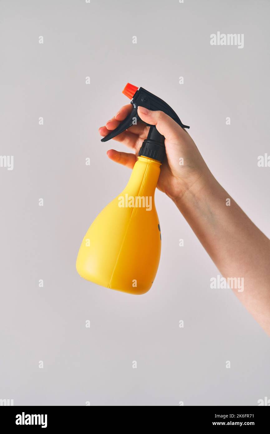 Eine junge Frau hält eine Sprühflasche in der Hand. Gelbe Sprühflasche auf weißem Hintergrund Stockfoto