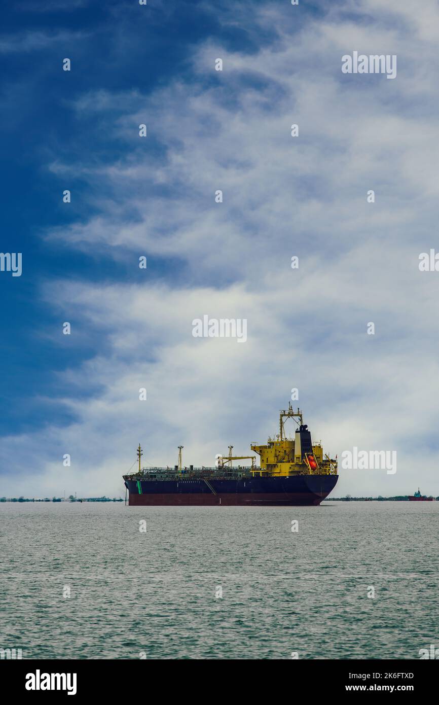 Tagesansicht eines festgetäuten Frachtschiffes an einem ruhigen Meer vor blauem Himmel mit dichten weißen Wolken. Stockfoto