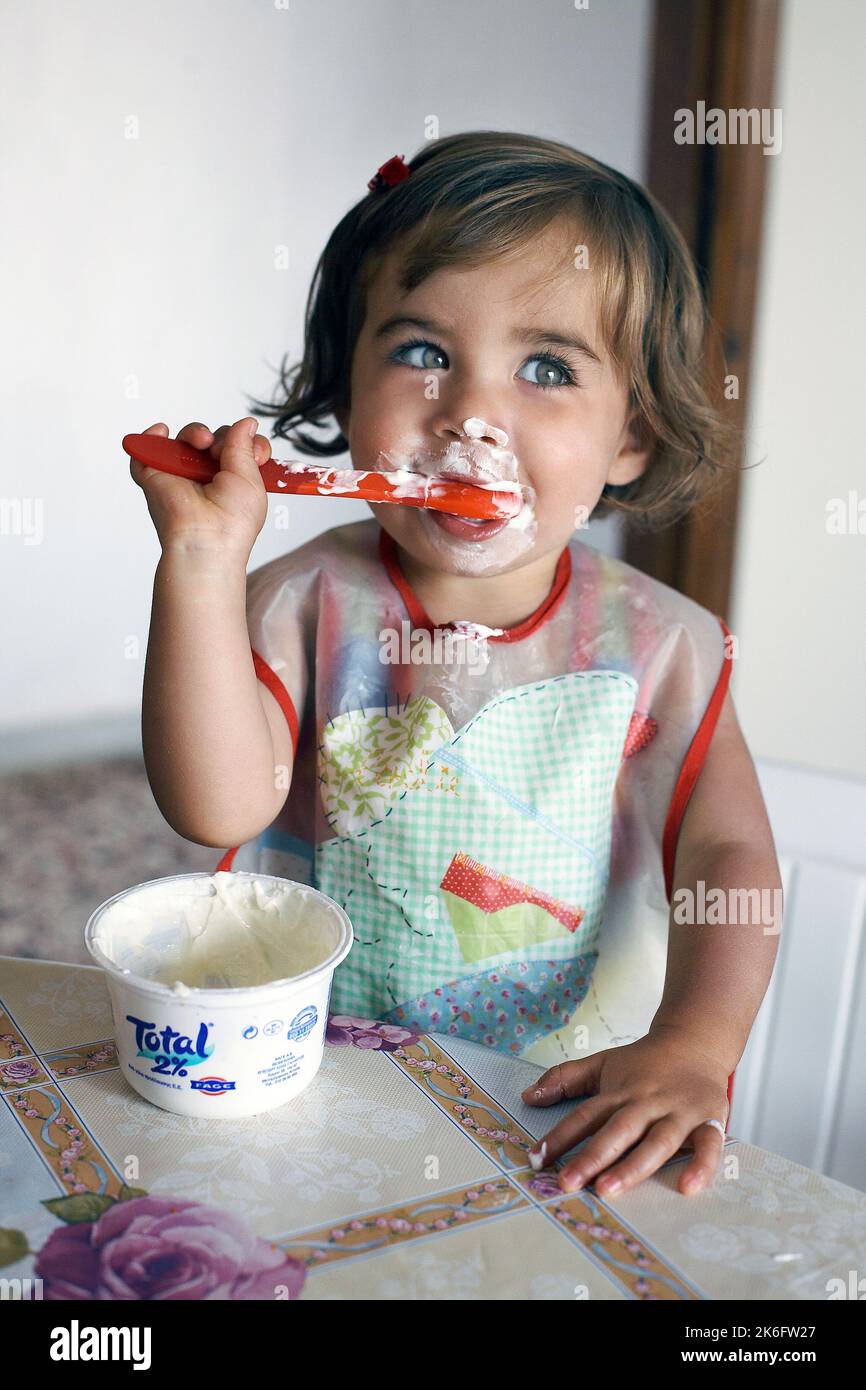 Niedliches Kleinkind Mädchen mit rotem Löffel isst Joghurt. Stockfoto