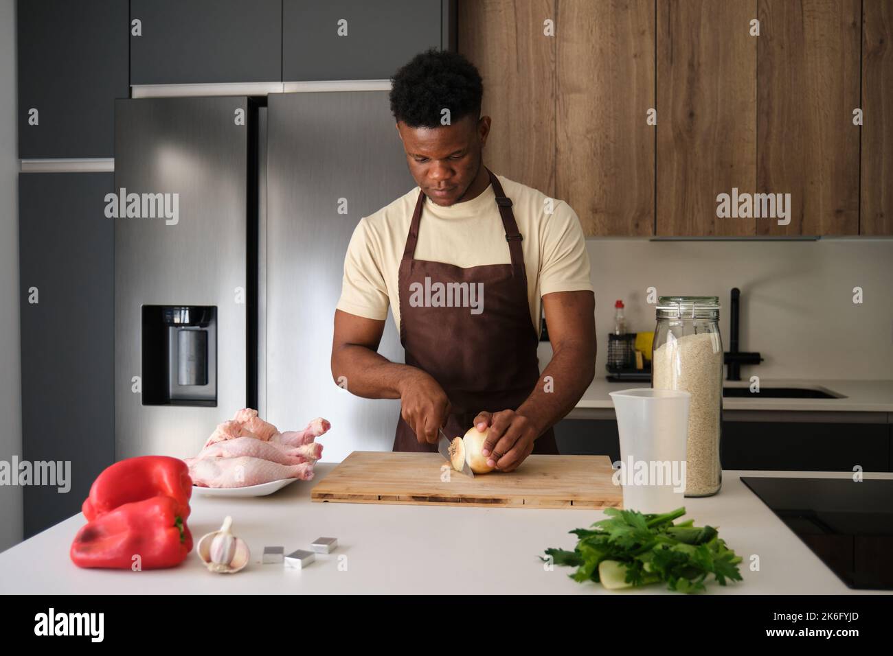 Junger schwarzer Mann schneidet Zwiebel, um Hühnerrezept vorzubereiten. Stockfoto