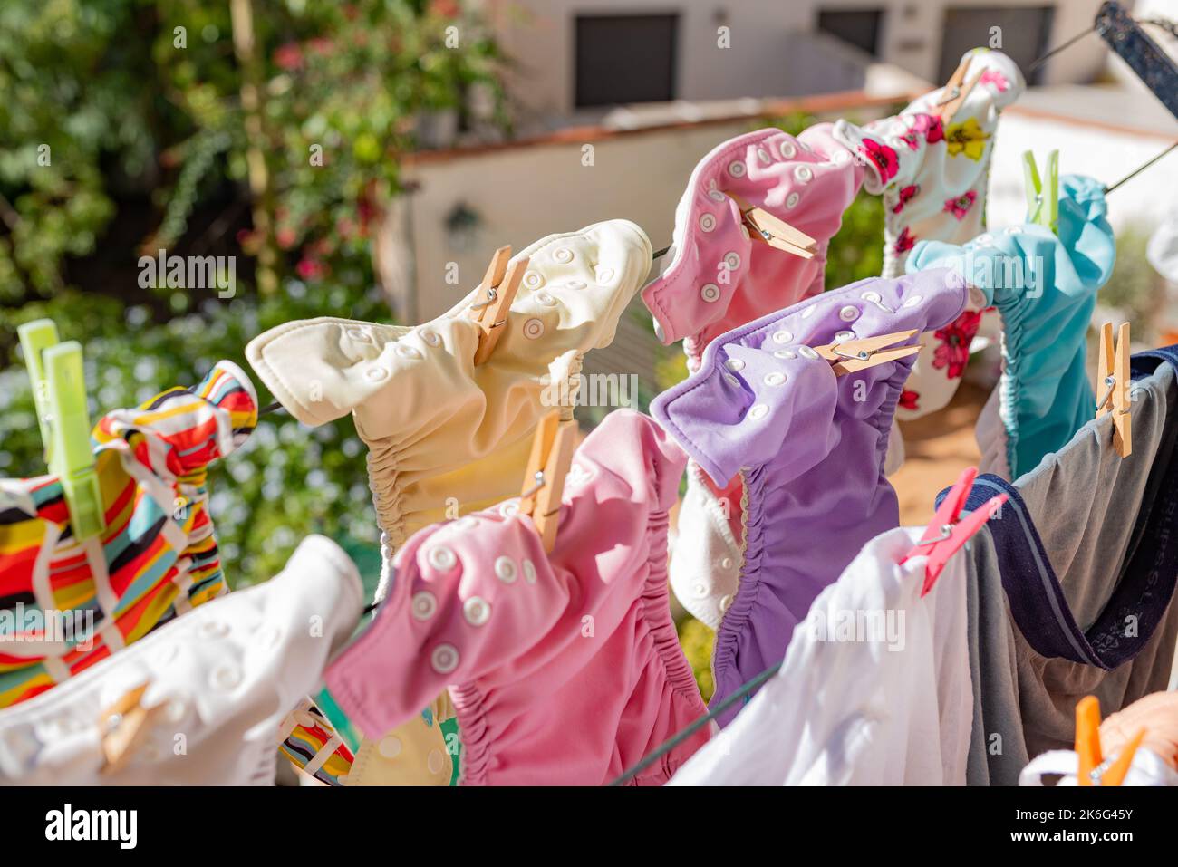 Stoffwindeln hängen beim Trocknen unter der Sonne an der Wäscheleine. Wäsche von bunten, wiederverwendbaren Windeln für Babys. Stockfoto