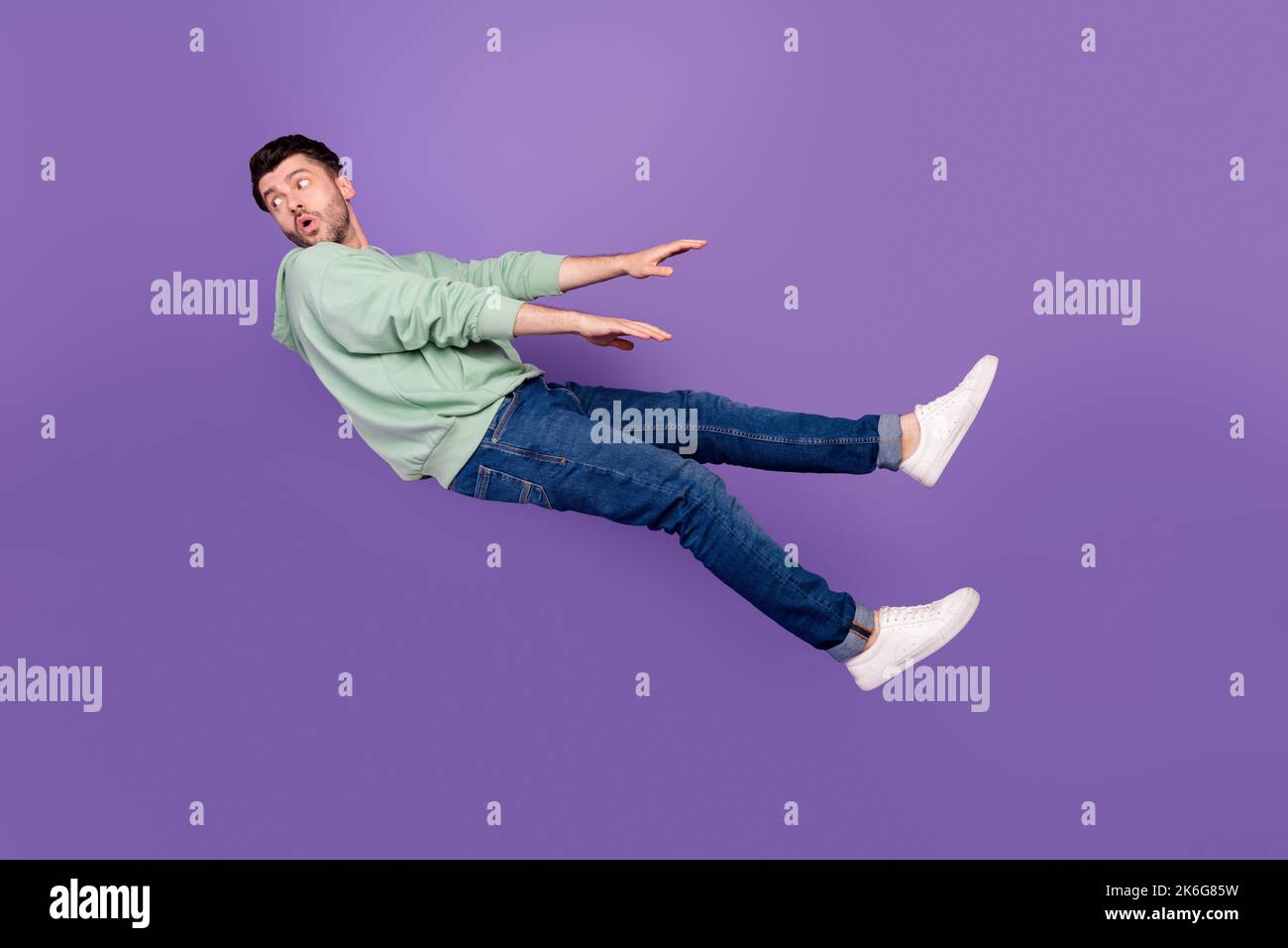 Ganzkörper-Foto von attraktiven jungen Mann Wind wegblasen Blick zurück gekleidet stilvolle khaki Kleidungsstück auf lila Hintergrund isoliert Stockfoto