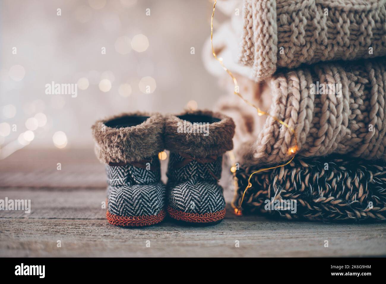 Stapel von gemütlichen Winter-Strickpullover, niedlichen kleinen Stiefeln und weihnachtsornamenten auf einem verschwommenen Hintergrund mit Bokeh. Warmes, Gemütliches Konzept. Speicherplatz kopieren Stockfoto