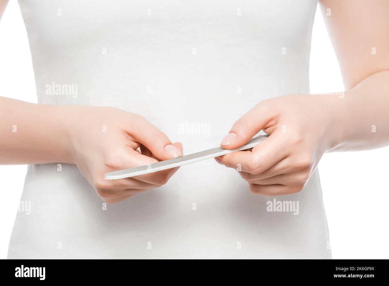 Ausgeschnittene Aufnahme einer Frau in einem weißen T-Shirt, das ihre Nägel feilt. Nahaufnahme, isoliert. Stockfoto