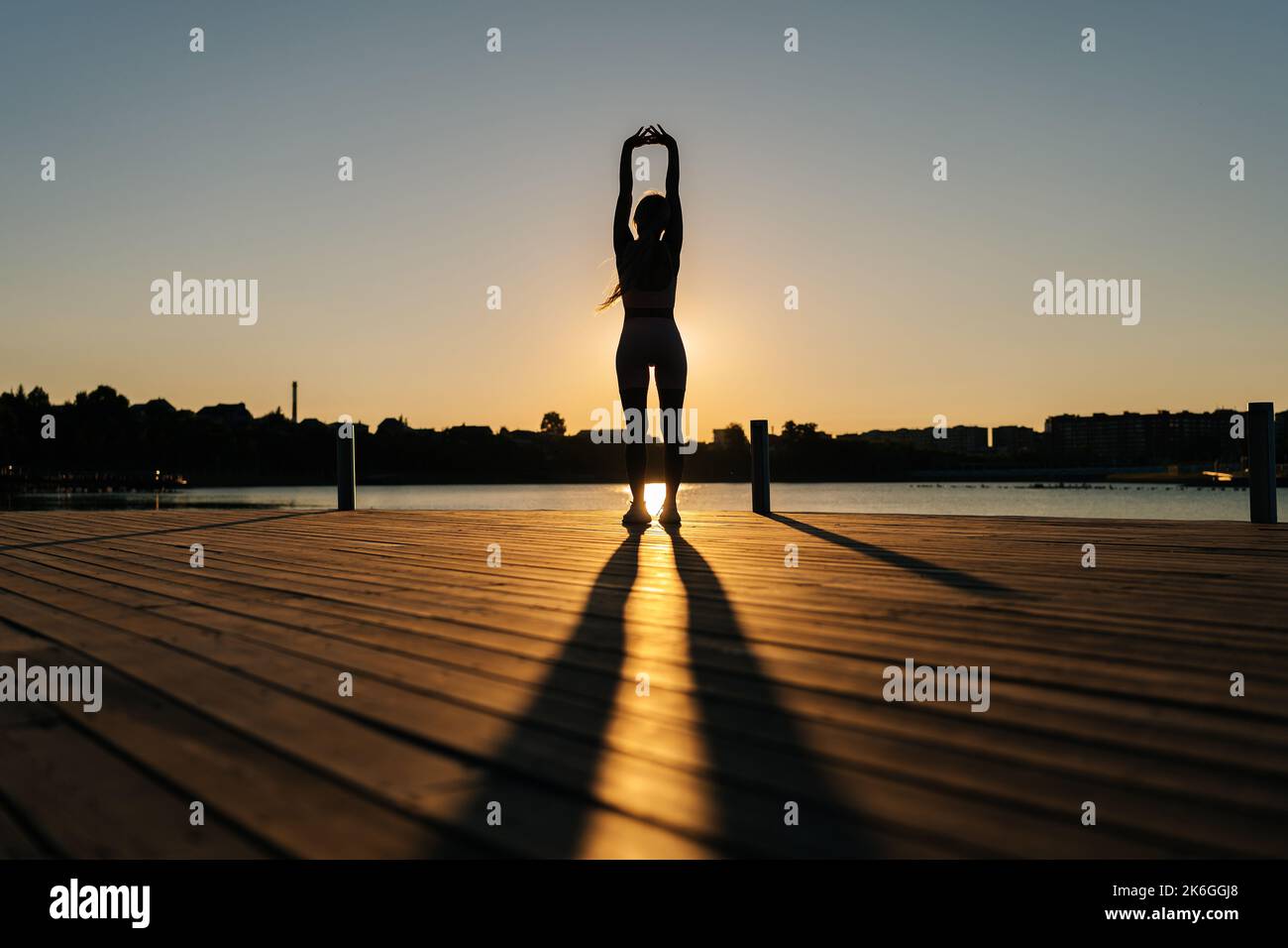 Silhouette einer nicht erkennbaren athletischen Frau in sportlichem Outfit, die die Armmuskeln aufwärmt und vor dem Laufen Dehnübungen übt. Stockfoto