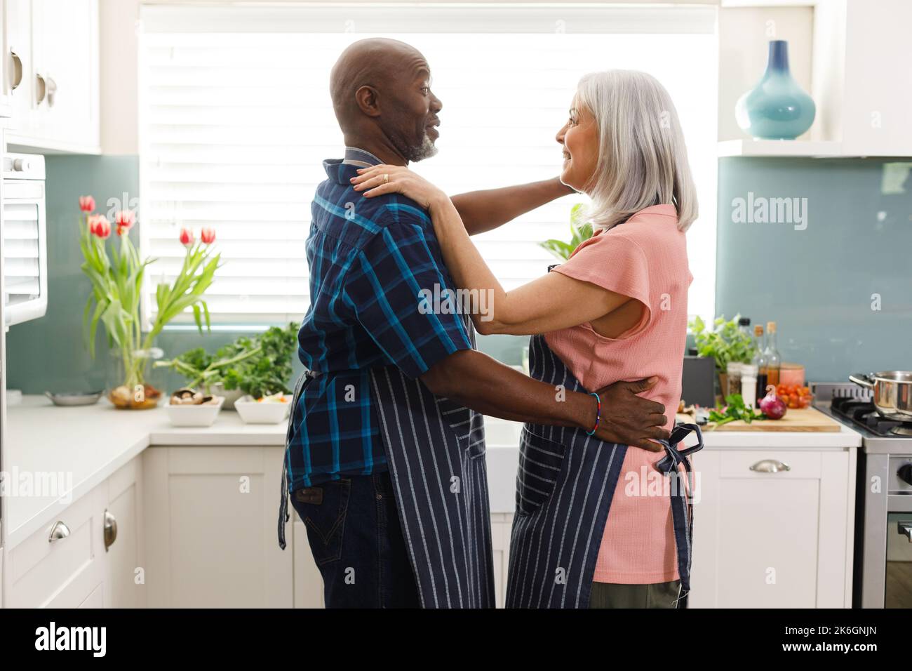 Glückliches, abwechslungsreiches Senior-Paar mit Schürzen und Tanz in der Küche Stockfoto