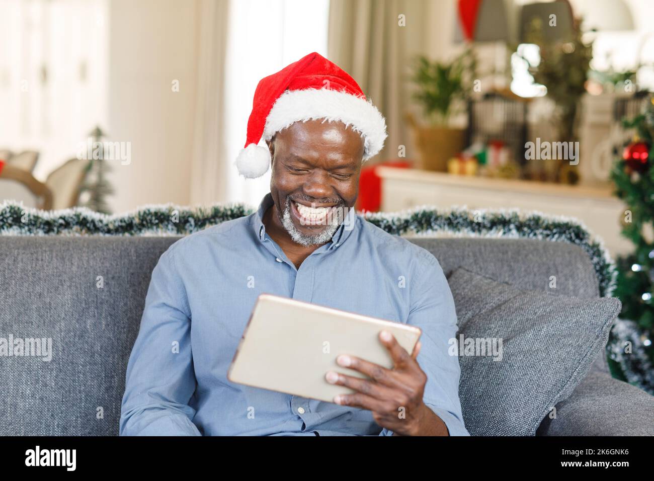 Glücklicher afroamerikanischer Senior-Mann mit weihnachtsmannmütze, der ein Tablet benutzt Stockfoto