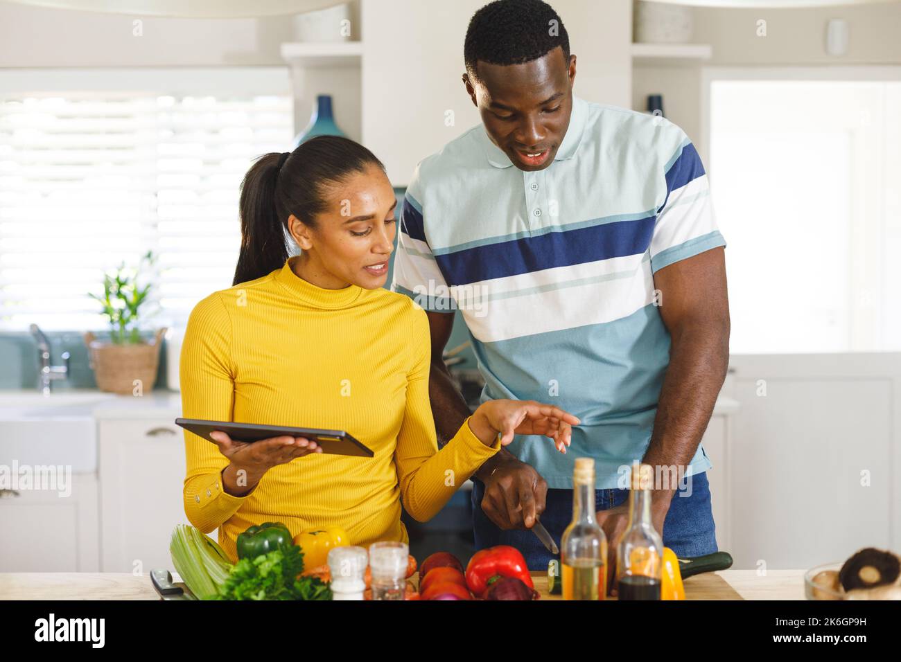 Glückliches, vielseitiges Paar, das das Rezept auf einem Tablet verwendet, um gemeinsam in der Küche Essen zuzubereiten Stockfoto