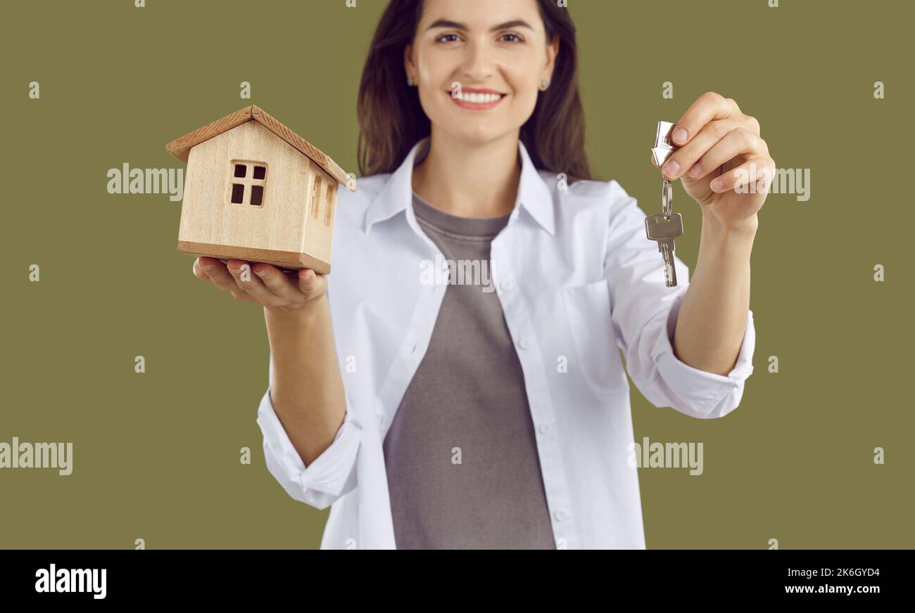 Eine Frau in einem weißen Hemd hält ein Holzmodell eines Hauses und die Schlüssel zum Haus. Stockfoto