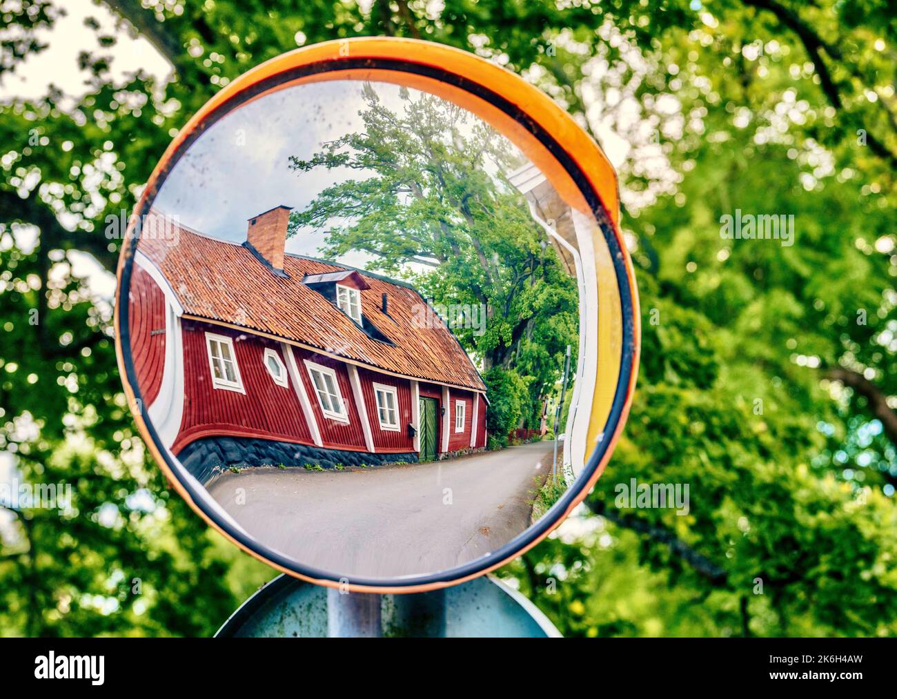 Eine Nahaufnahme eines roten Hauses spiegelt sich in einem sphärischen Straßenspiegel wider Stockfoto