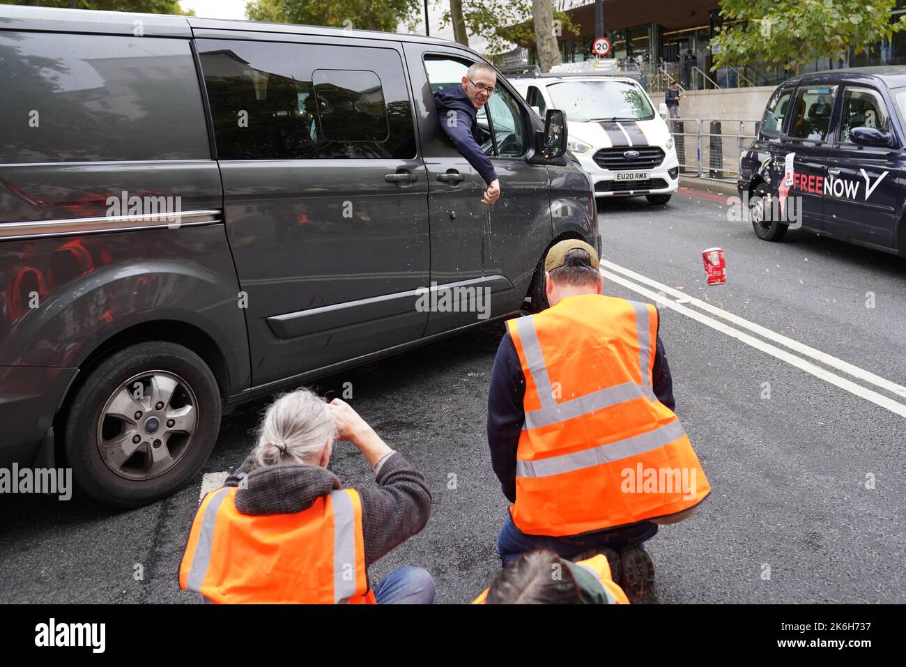 Ein Fahrer wirft einen Drink auf die Demonstranten von Just Stop Oil vor dem New Scotland Yard in London. Bilddatum: Freitag, 14. Oktober 2022. Stockfoto