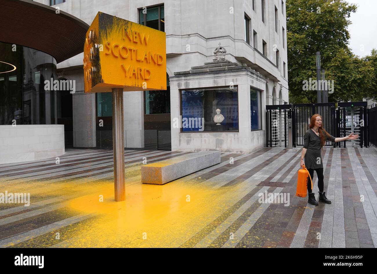 Ein „Just Stop Oil“-Protestler steht neben einem Schild, das sie vor dem New Scotland Yard in London besprüht hat. Bilddatum: Freitag, 14. Oktober 2022. Stockfoto