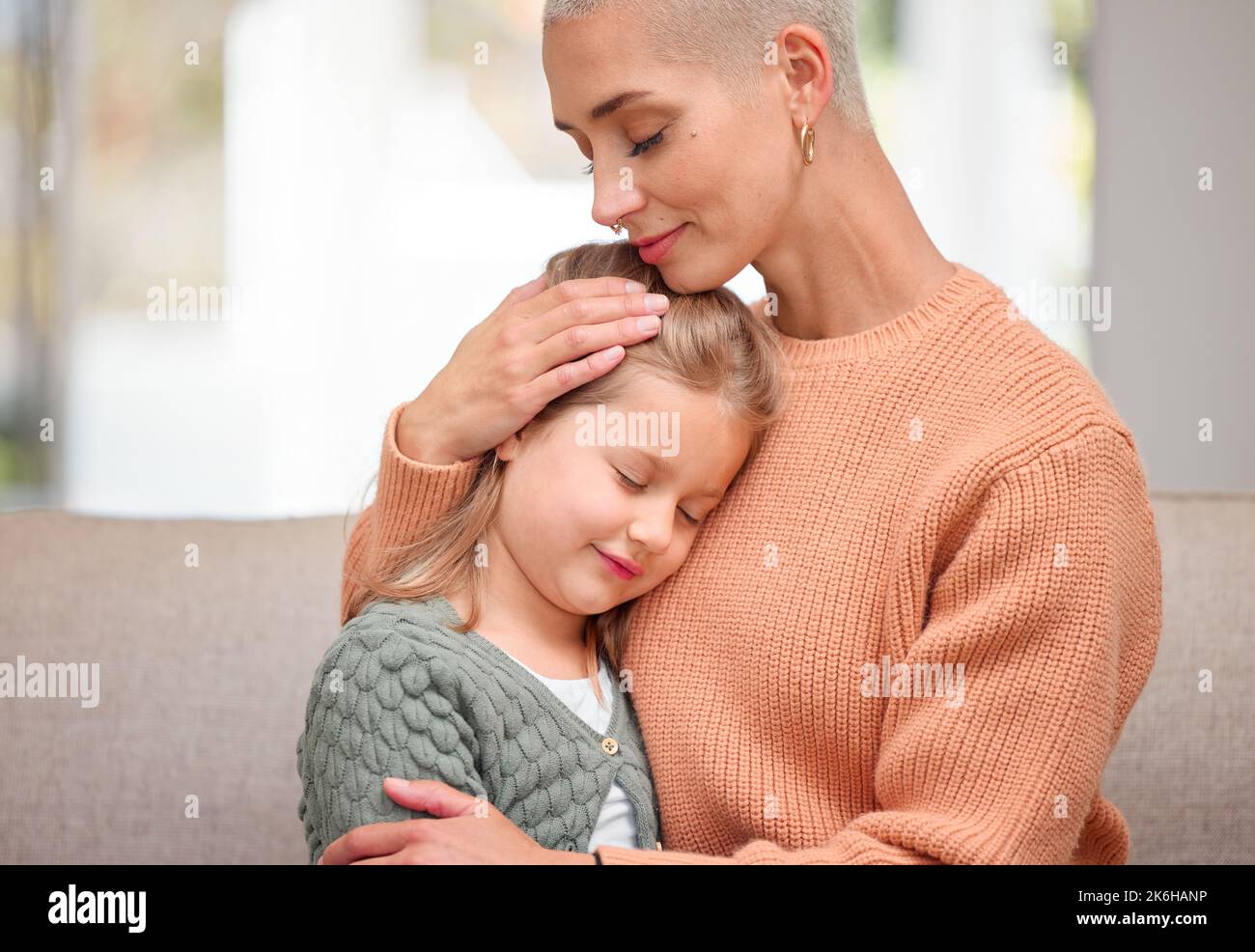 Mütter spüren ihre Kinder am tiefsten Schmerzen. Eine junge Mutter tröstet ihre Tochter zu Hause auf dem Sofa. Stockfoto