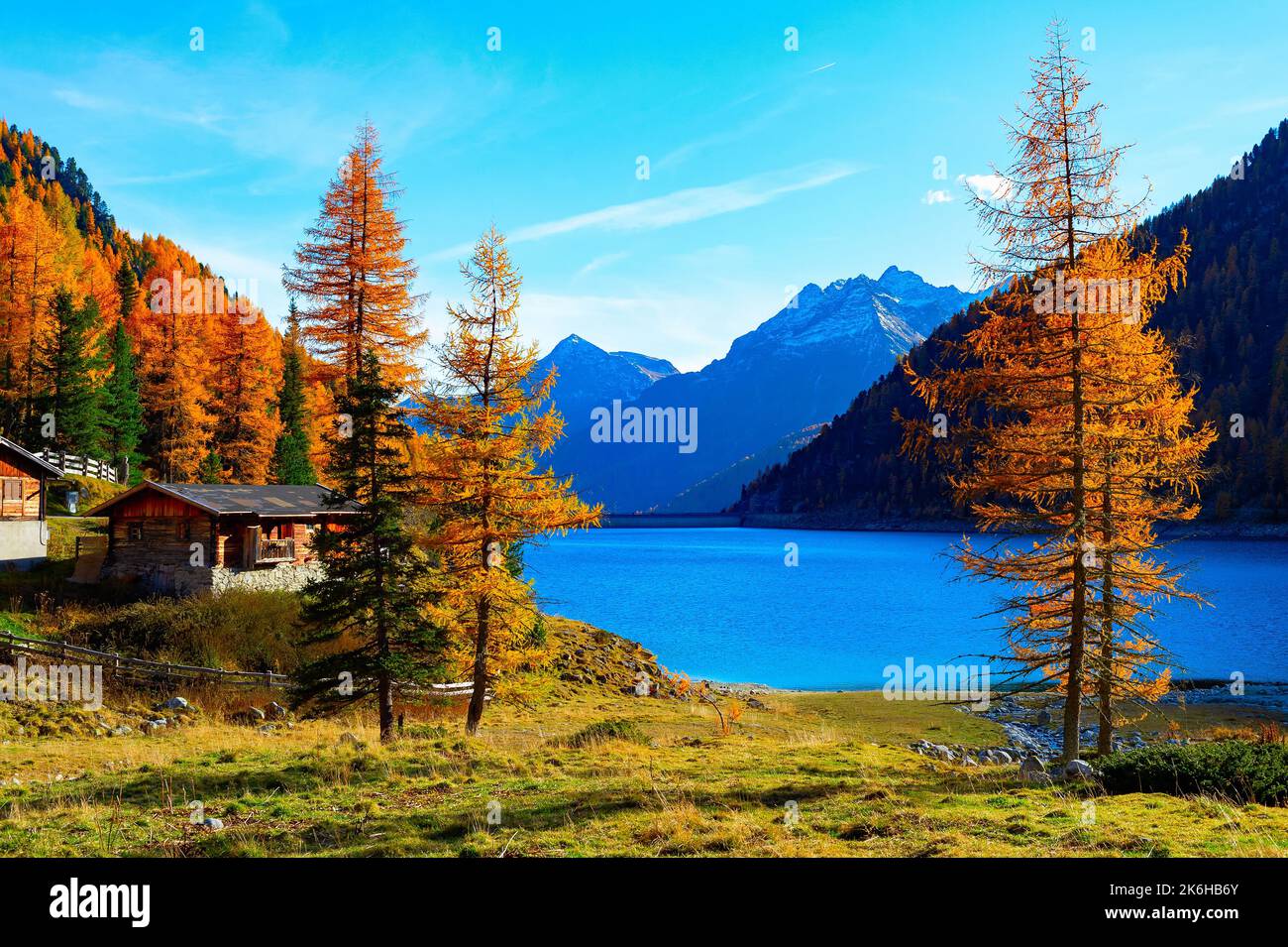 Bunte Herbstlandschaft mit Hütten am See, goldenen Bäumen und Alpen im Hintergrund, Österreich Stockfoto