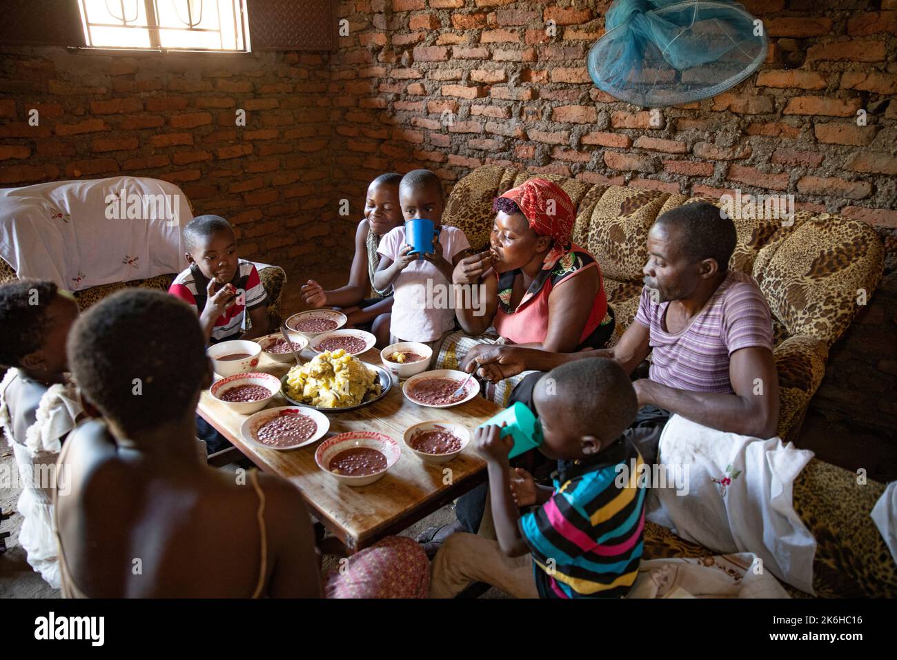 Ugandische Familie, die in ihrem Haus im Kasese District, Uganda, Ostafrika, eine Mahlzeit mit Bohnen und pürierten herzhaften Bananen gemeinsam hat. Stockfoto