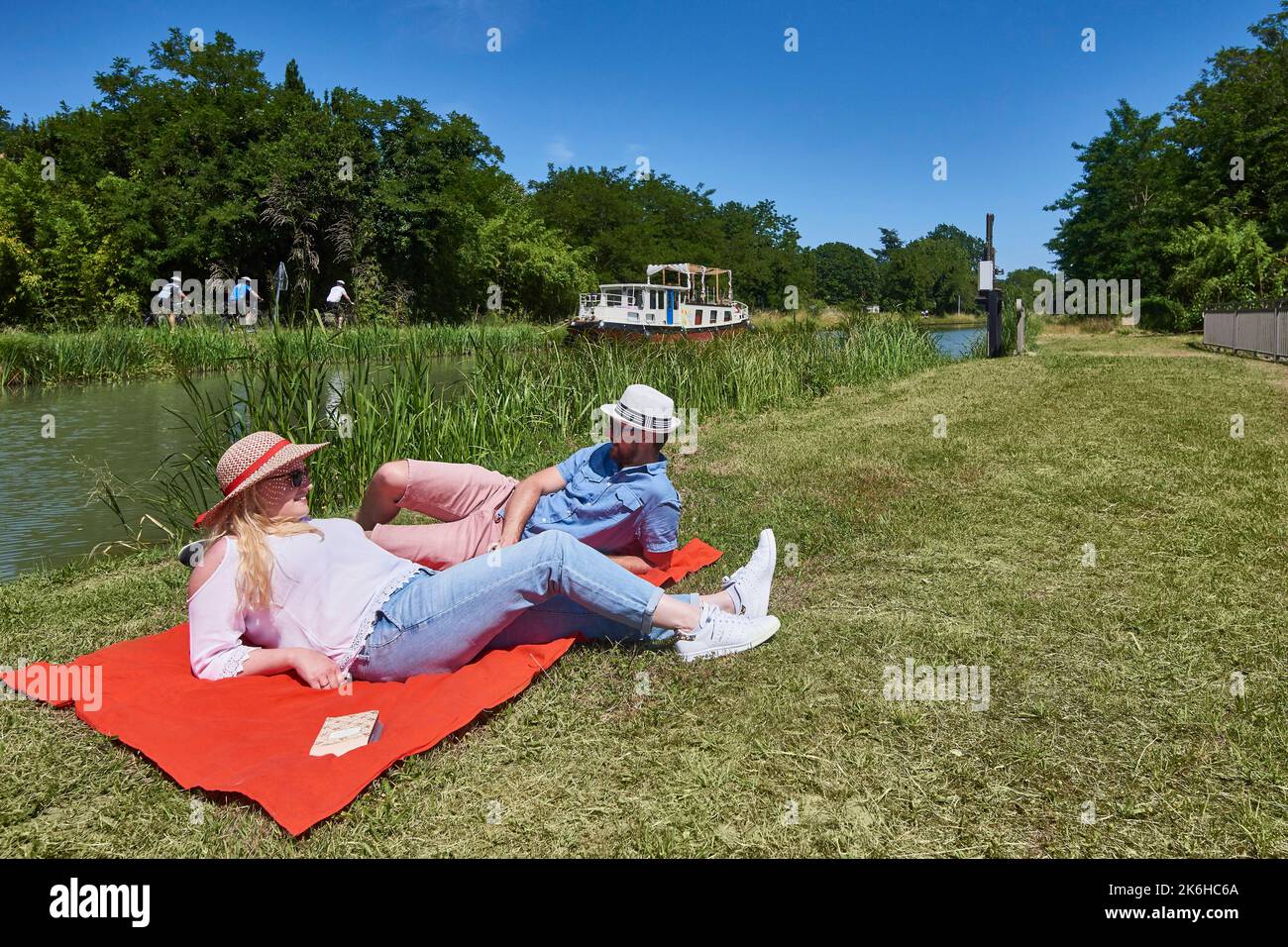 Ein Paar, das eine Pause macht, sich entspannt und am Canal du Midi in der Nähe des Schleusenwärterhauses in Saint Jean de Thurac (Südwestfrankreich) liest. Mann und Stockfoto