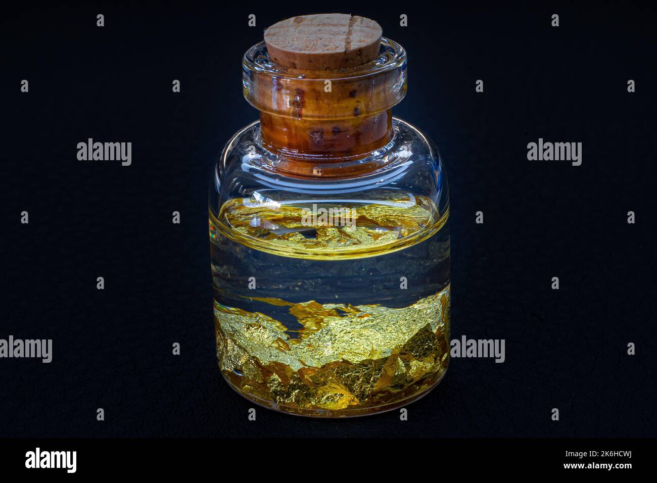 Eine kleine Glasflasche mit einem Holzkorken auf einer schwarzen Oberfläche mit 22 Karat Gold lässt Makro aus nächster Nähe Stockfoto