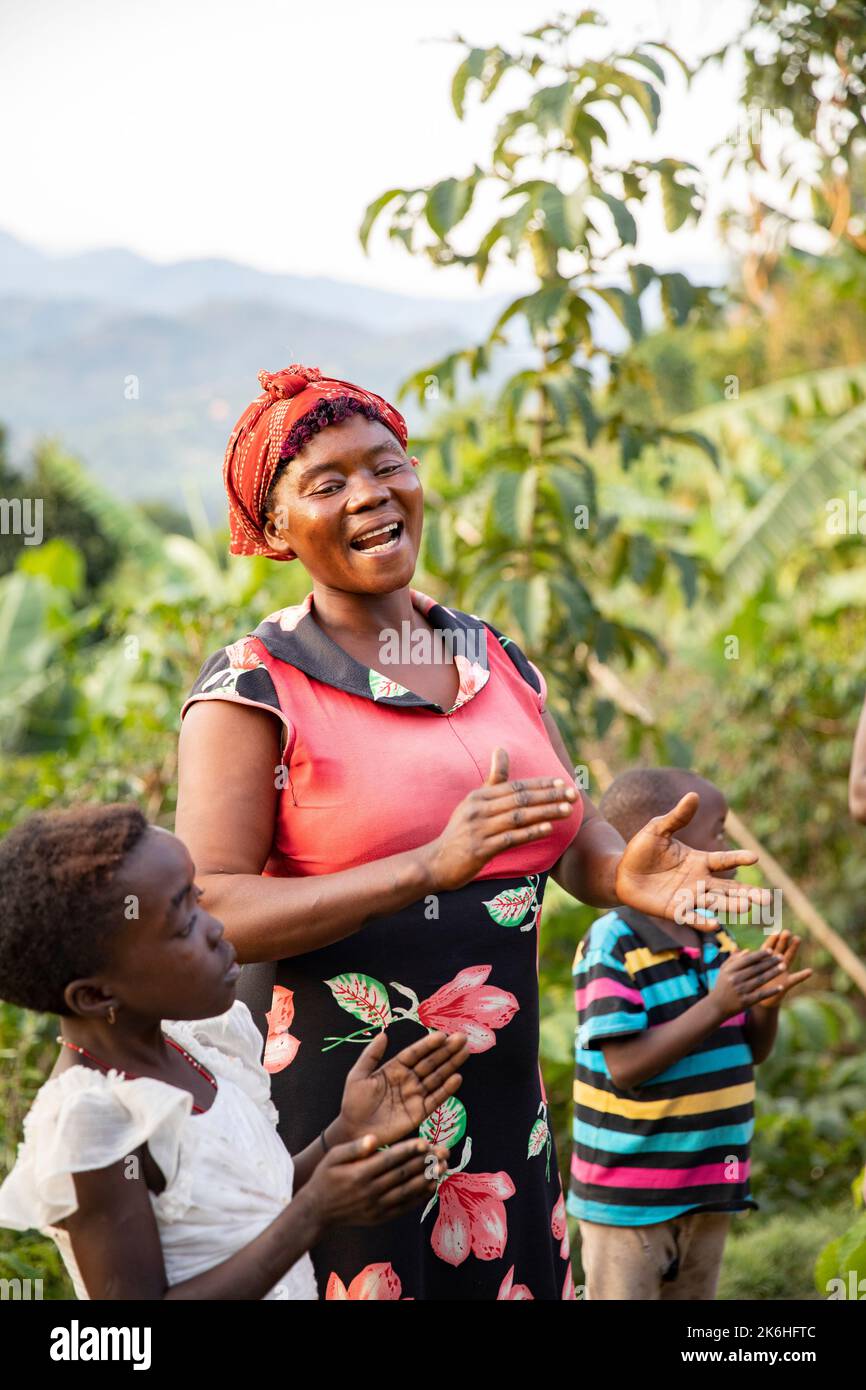 Eine glückliche Afrikanerin singt mit ihrer Familie vor ihrem Haus in Ugandas Rwenzori Mountains, Kasese District, Ostafrika. Stockfoto