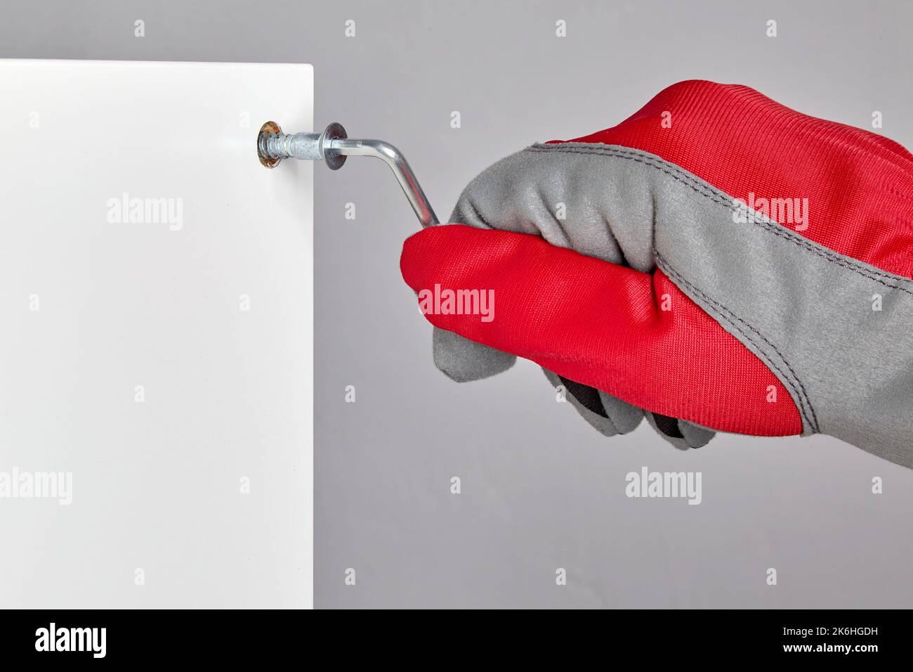 Eine Person in einem roten Schutzhandschuh schraubt eine Bestätigung in ein Loch in einem Möbelbrett Stockfoto