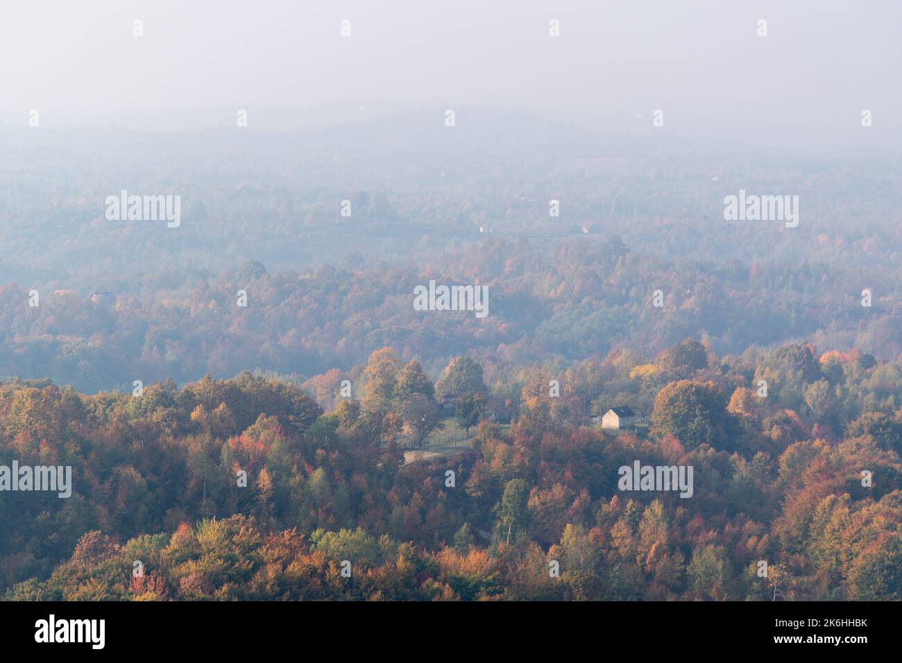 Einsames Haus auf einem Hügel, umgeben von üppigem Wald in herbstlichen Farben, ferne Hügel verblassen im Morgennebel Stockfoto