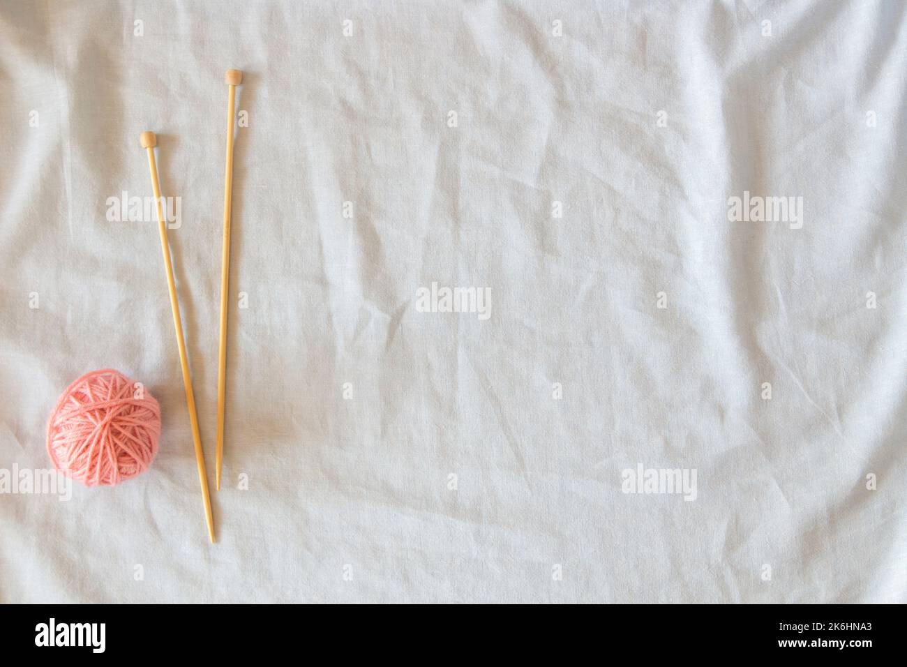 Rosa Fadenkugel mit hölzernen Bambusstricknadeln auf weißem Leinenstoff-Hintergrund. Draufsicht, Kopierbereich. Hobby, Entspannung, psychische Gesundheit Stockfoto