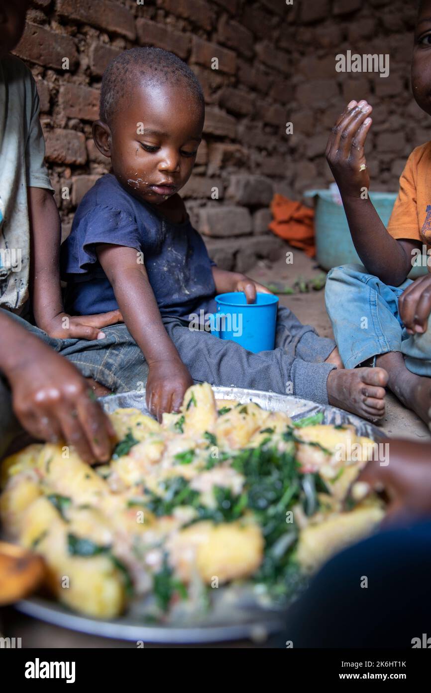 Eine Gruppe afrikanischer Kinder essen eine Mahlzeit aus stärkehaltigen Bananen und Gemüse mit Erdnusssauce in ihrem Haus im Kasese District, Uganda, Ostafrika. Stockfoto