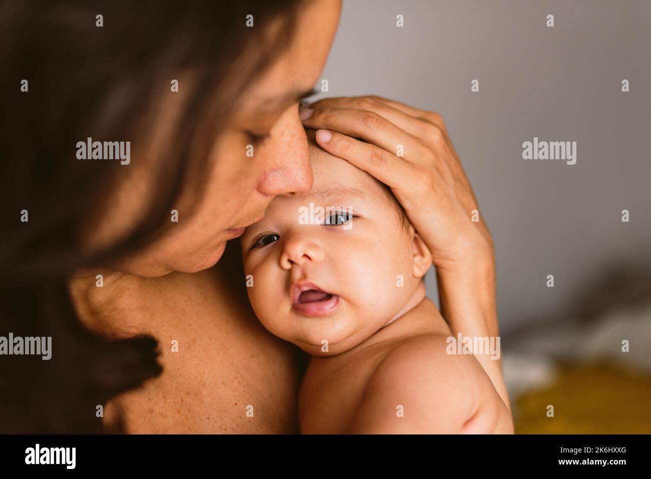 Intimes Porträt einer hispanischen Mutter, die ihre neugeborene Tochter in den Armen hält und Liebe und Fürsorge zeigt, mit weichem, natürlichem Licht. Konzept der Verklebung und Stockfoto