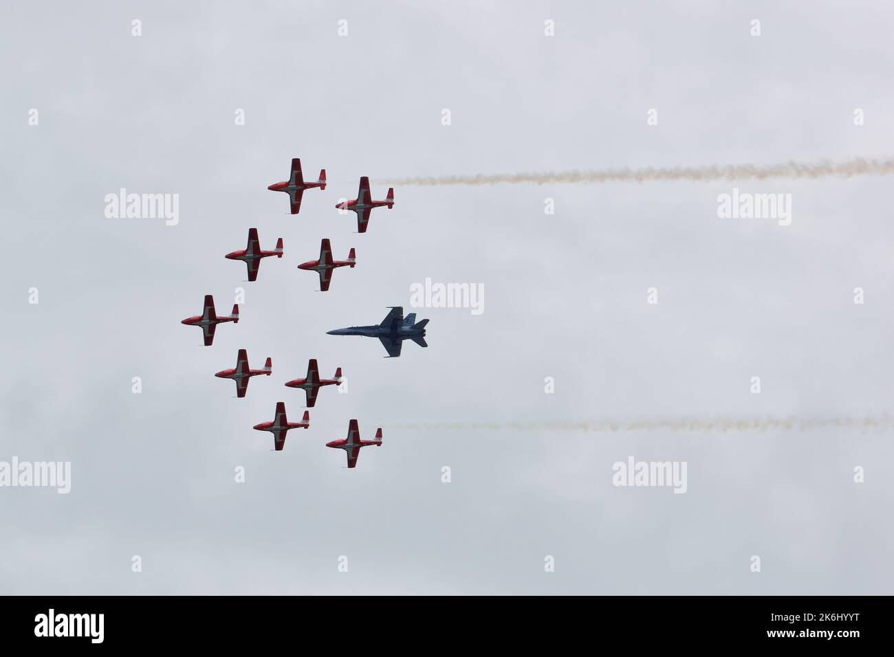 RCAF Snowbirds fliegen in Formation, zusammen mit einem Kampfjet. Zwei Rauchströme auf beiden Seiten der Formation. Stockfoto