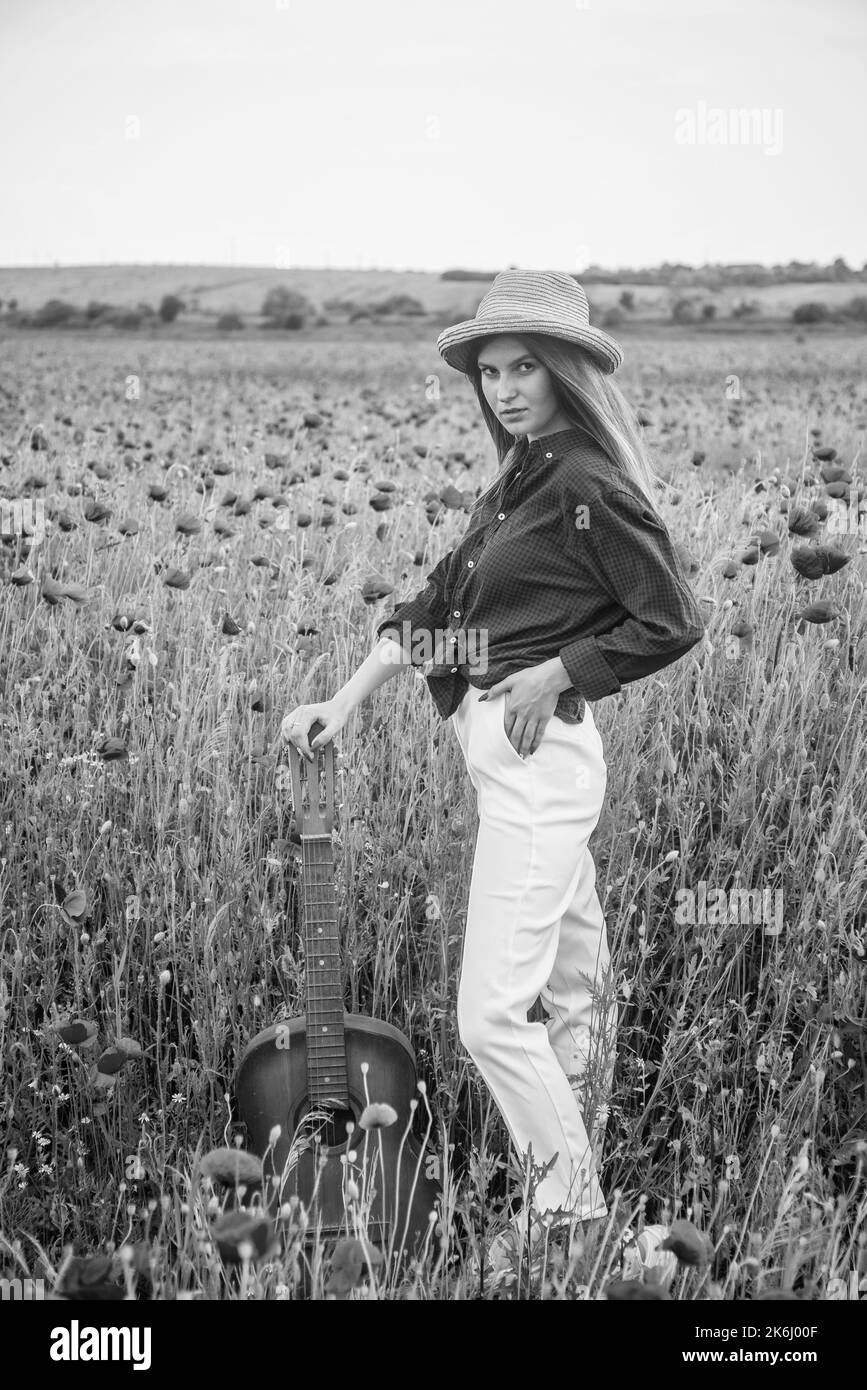 Frühling auf dem Land. lady tragen kariertes Hemd und Hut in Blumenfeld. Country-Musik-Sängerin. Frau in Mohn Feld mit Akustikgitarre. Sommerblume Stockfoto