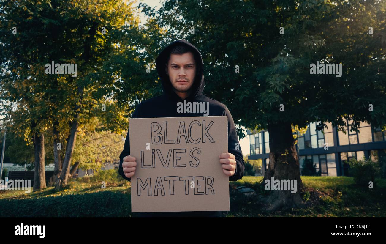 Junger Aktivist in Kapuzenpullover mit Plakat mit Schriftzug „Black Lives Matter“ außen, Stockbild Stockfoto